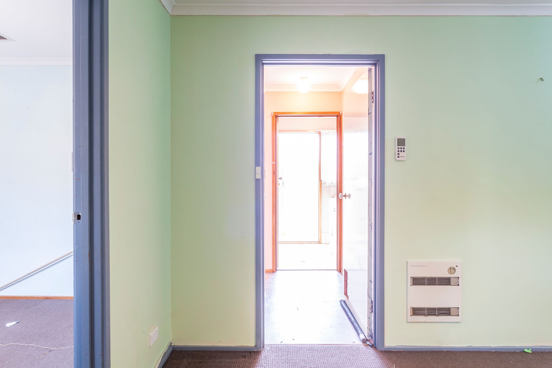 Empty interior room with light green walls, brown carpet, and three open doorways.