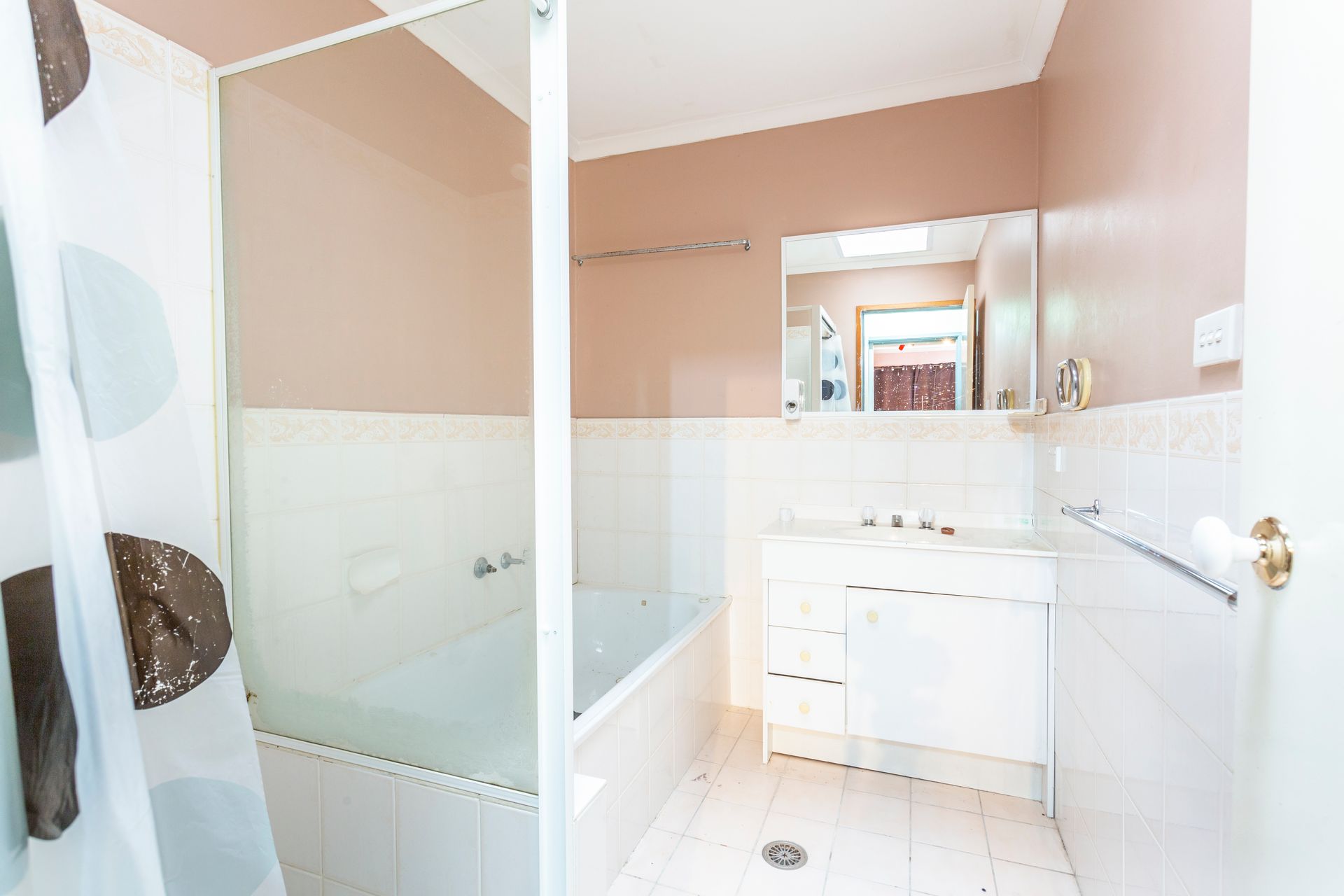 Bathroom with white tiles, bathtub, shower curtain, white vanity, and mirror. Pink walls.