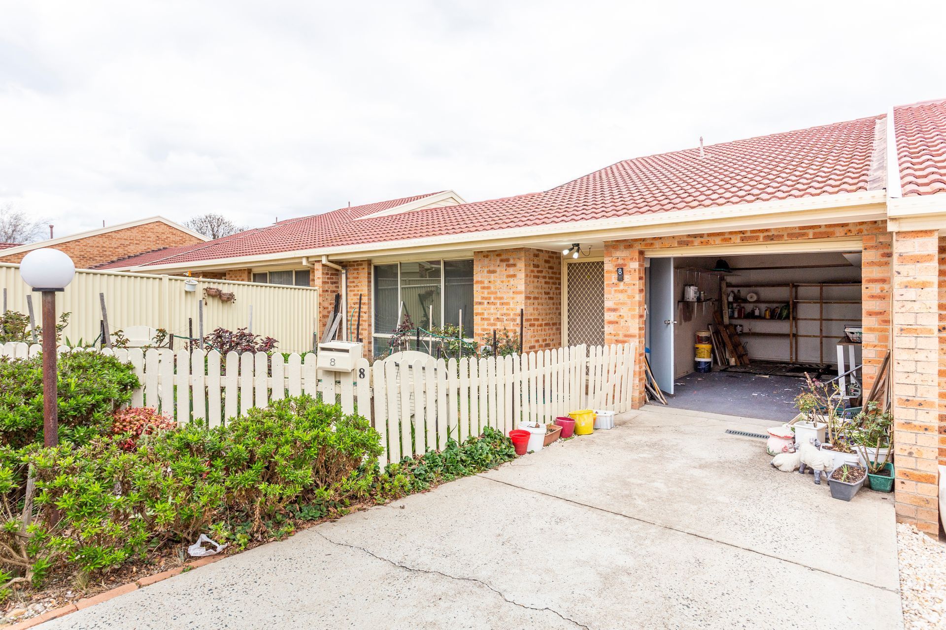 Brick townhouse with red-tiled roof, white picket fence, driveway, and open garage.
