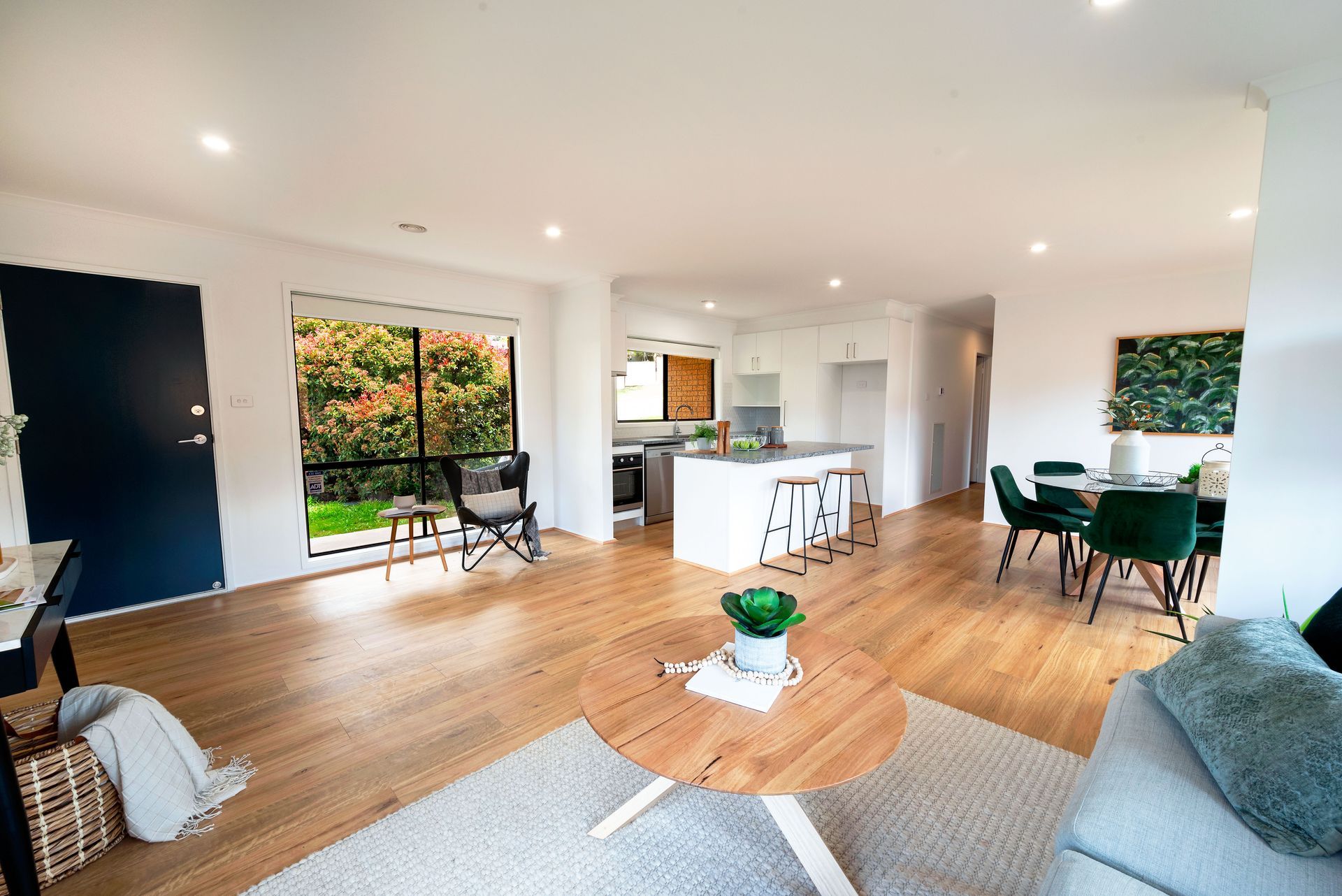 Living room with hardwood floors, a round coffee table, and a dining table with green chairs.