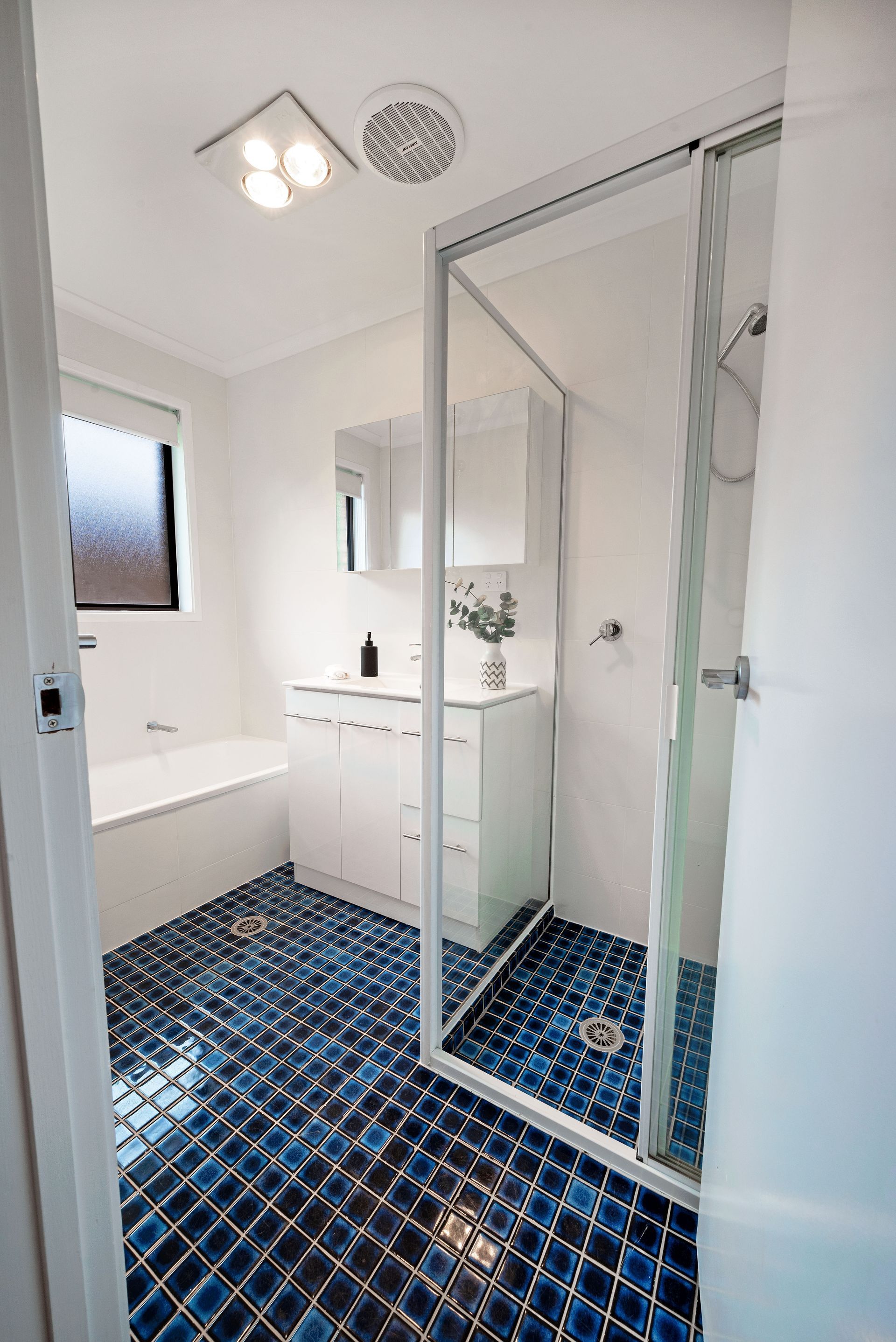 Blue-tiled bathroom with a glass shower, white vanity, and a bathtub near a window.