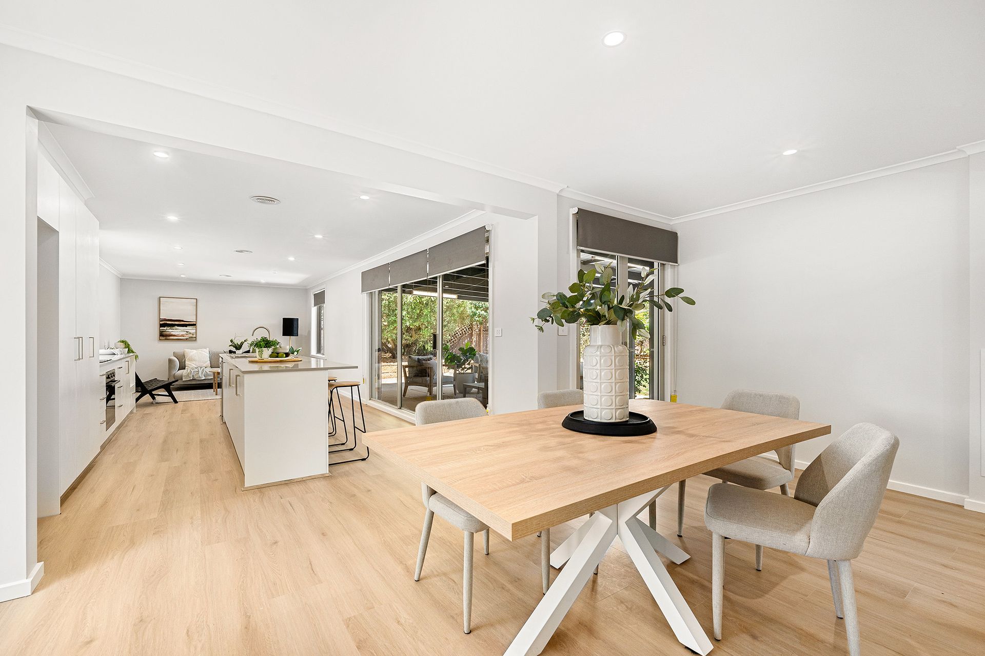 Dining area with wooden table, chairs, and open view to a kitchen with a white island.