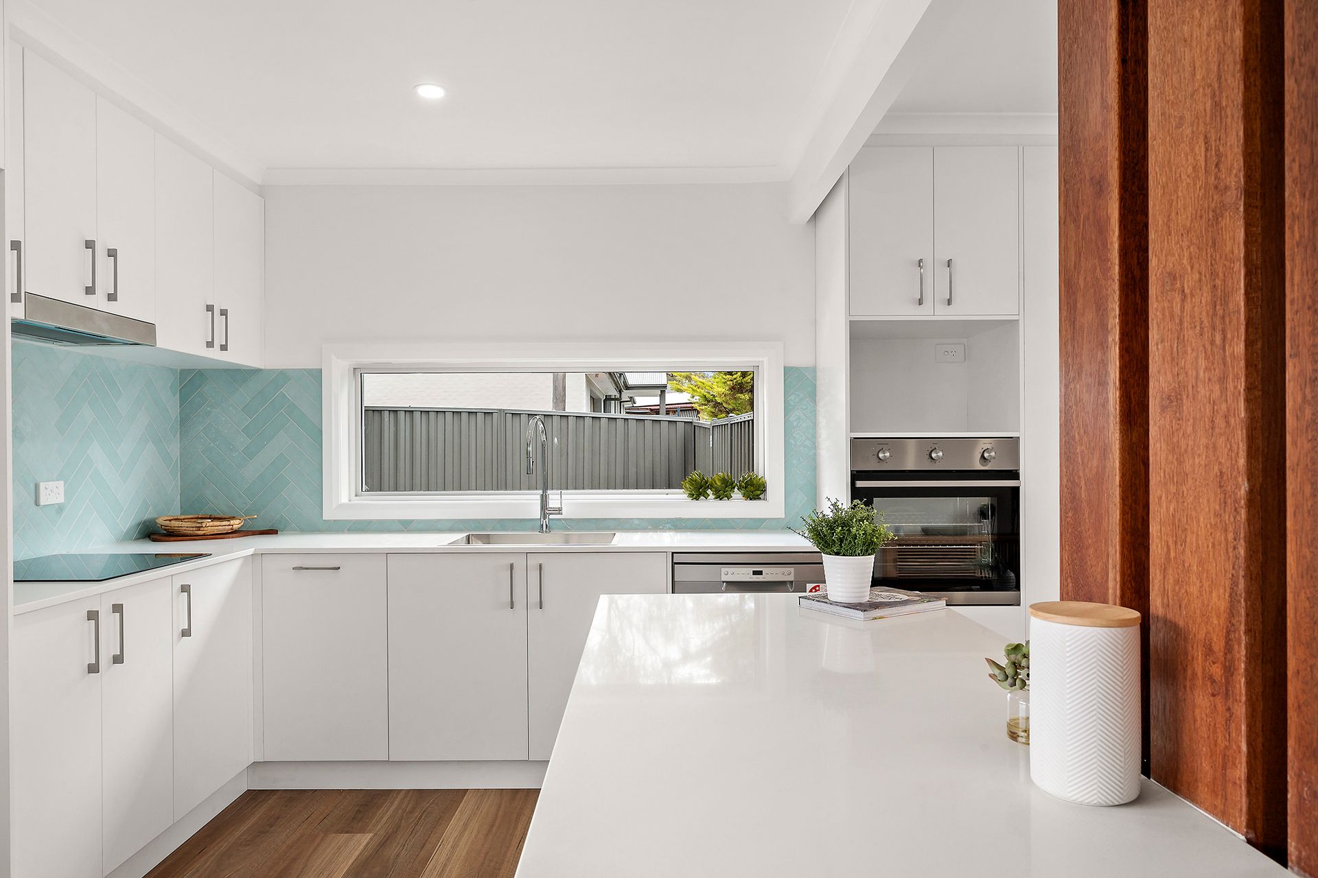 White laundry room with sink, counter, cabinets, and door to outside. Plant and laundry basket are present.