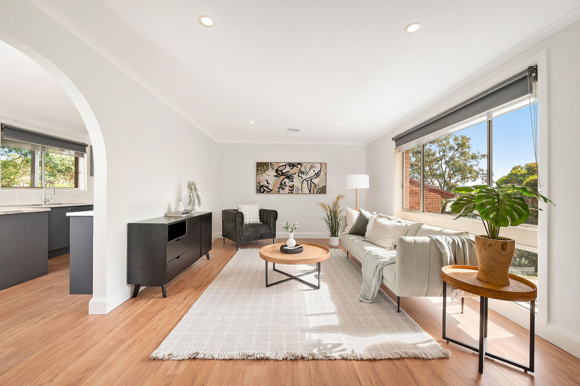Living room with white walls, wooden floor, gray furniture, and large window.