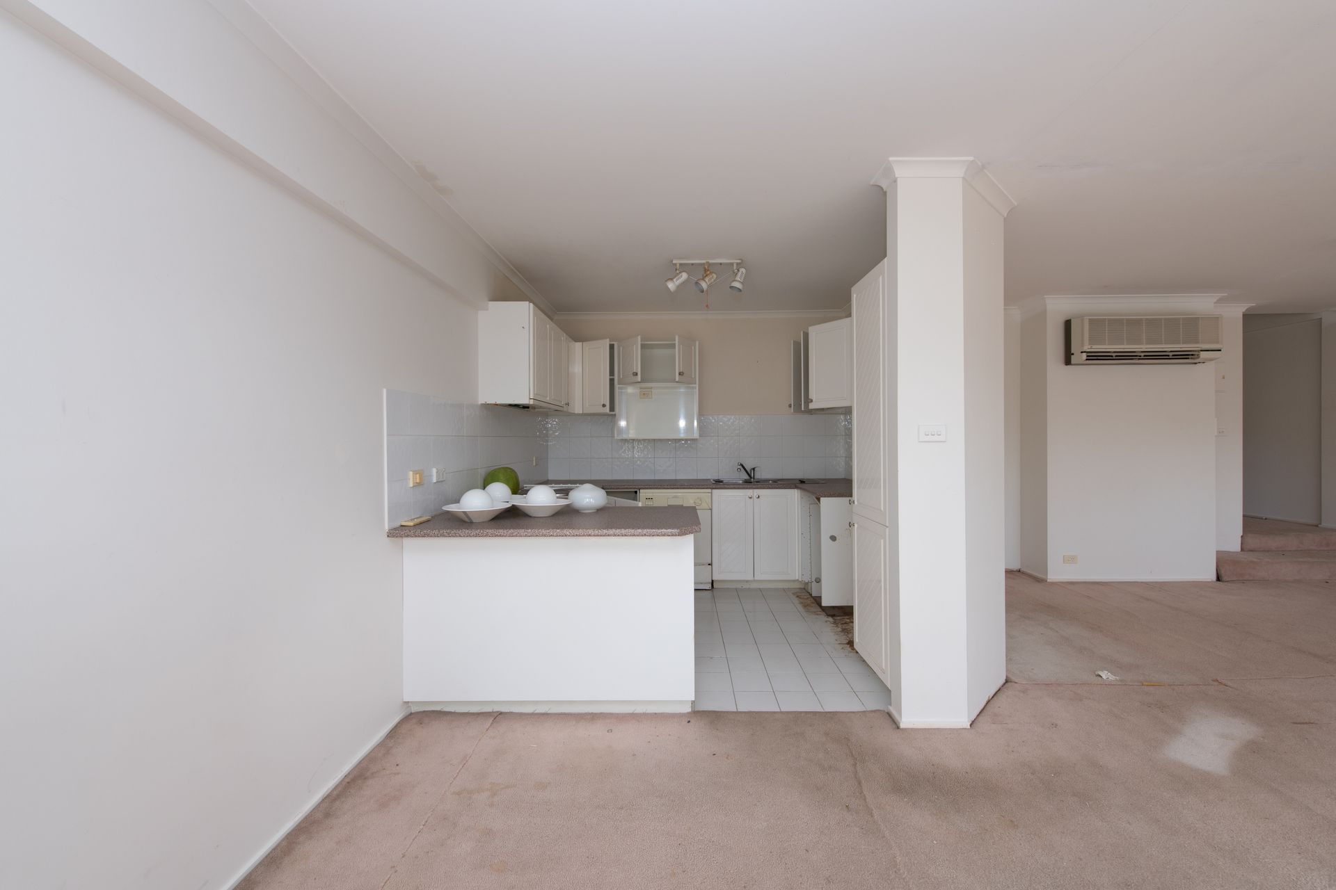 Small white kitchen with countertop and cabinets, in a neutral-toned apartment, light flooding the space.