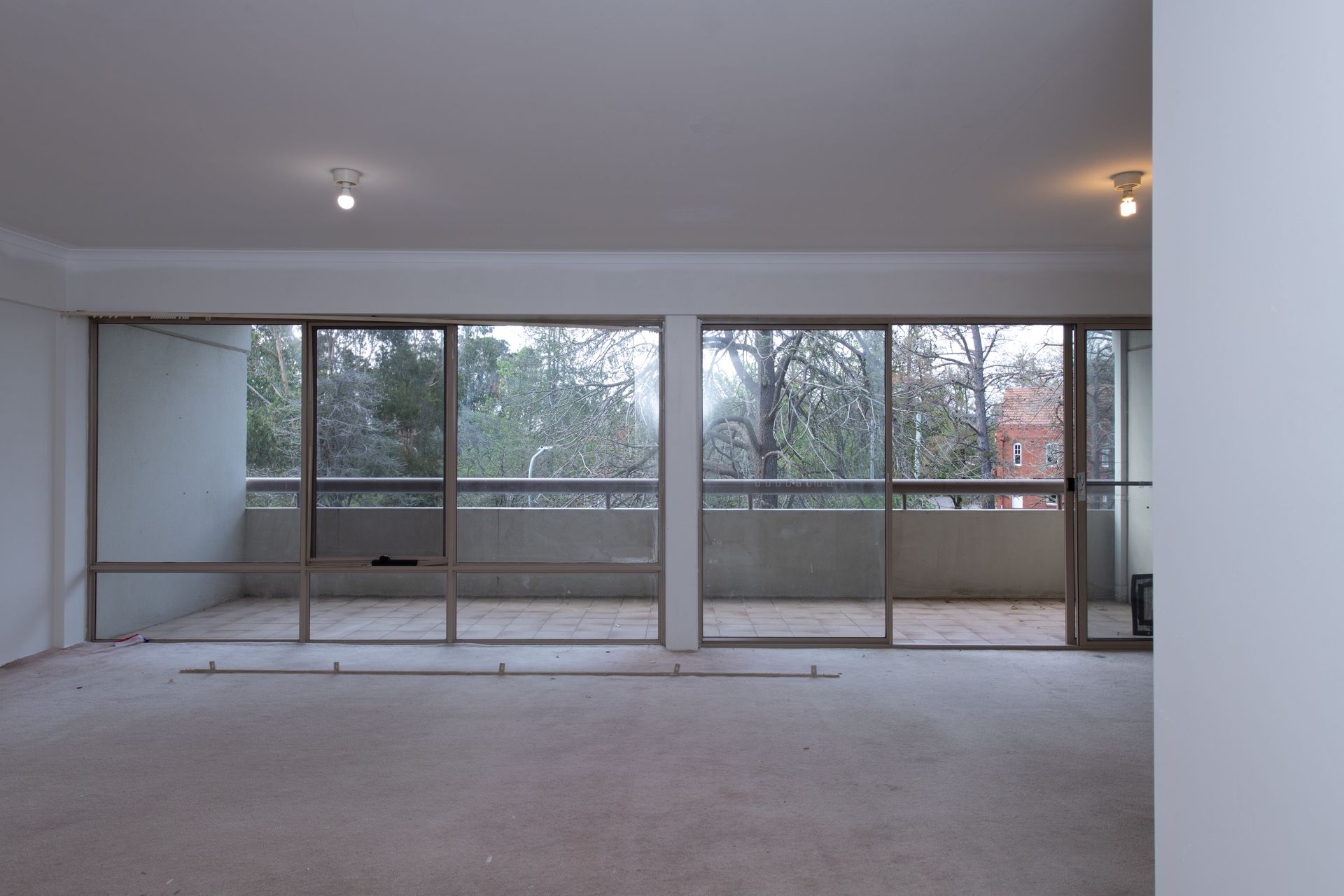 Empty room with large sliding glass doors leading to a balcony with trees visible outside.