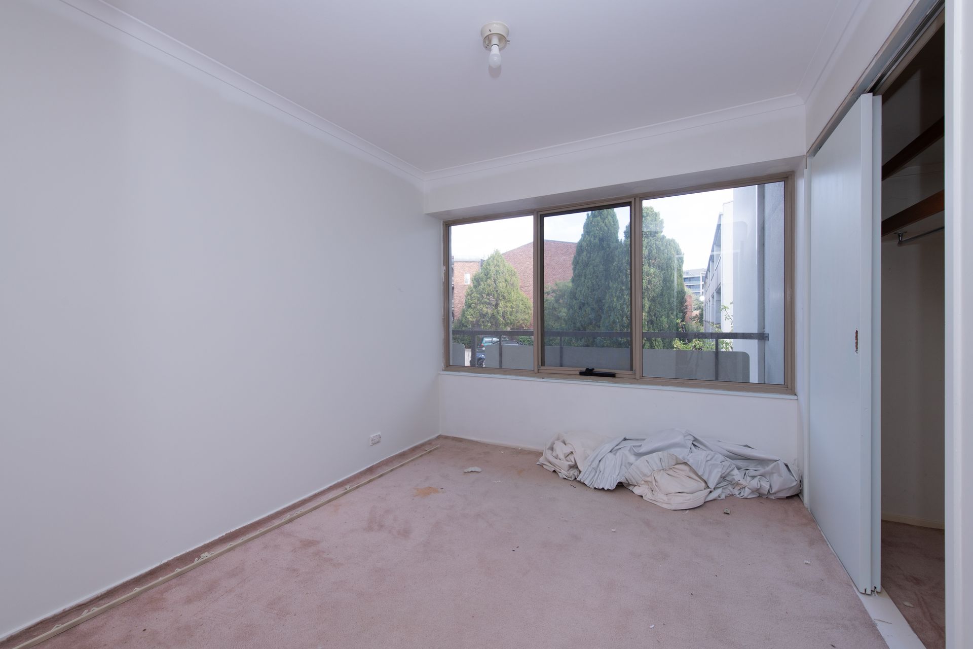 Empty room with large sliding glass doors leading to a balcony with trees visible outside.