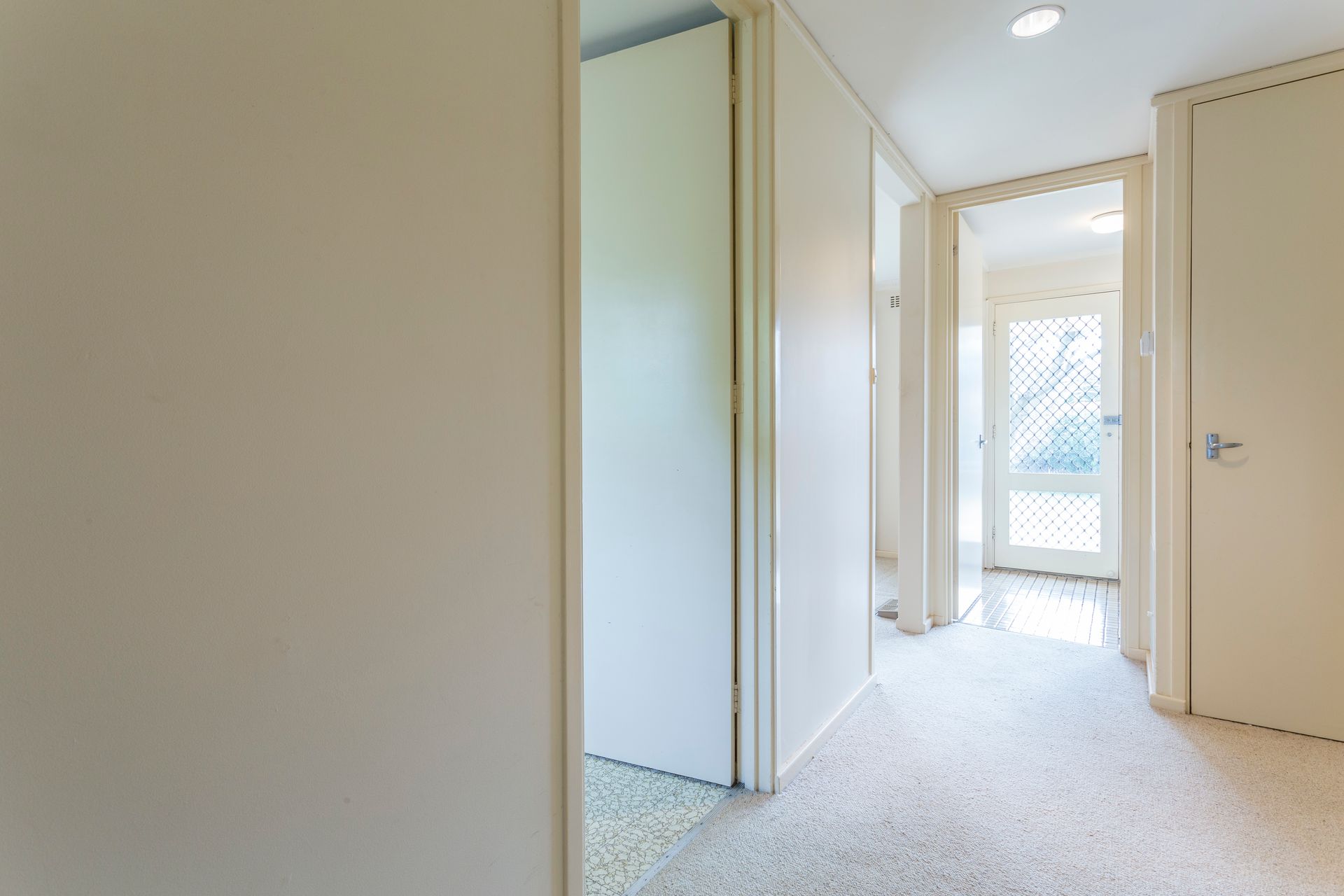 Hallway with beige walls, doors, and a light-colored carpet leading to an exterior glass door.