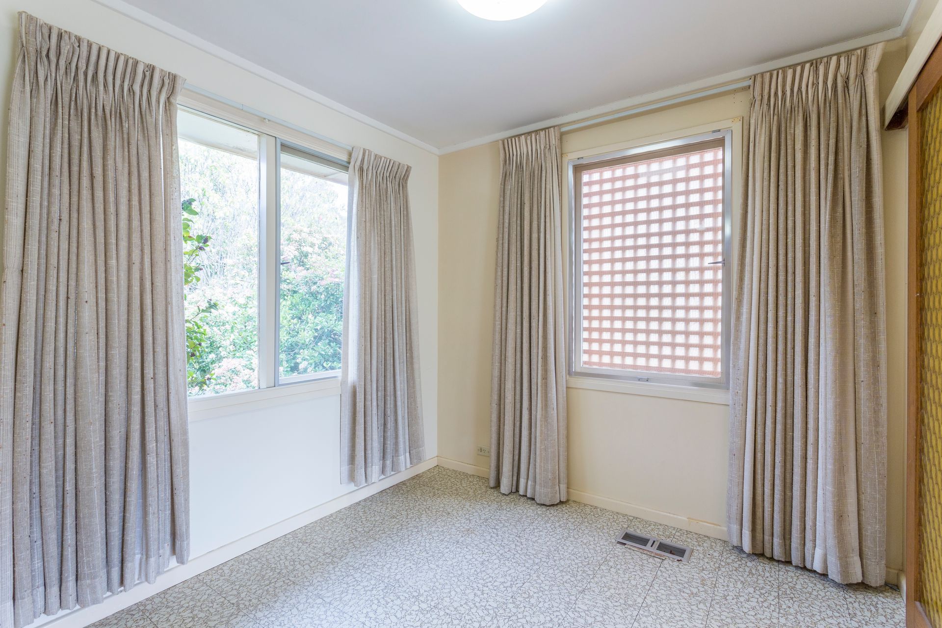 Empty room with two windows and beige curtains; beige carpet.