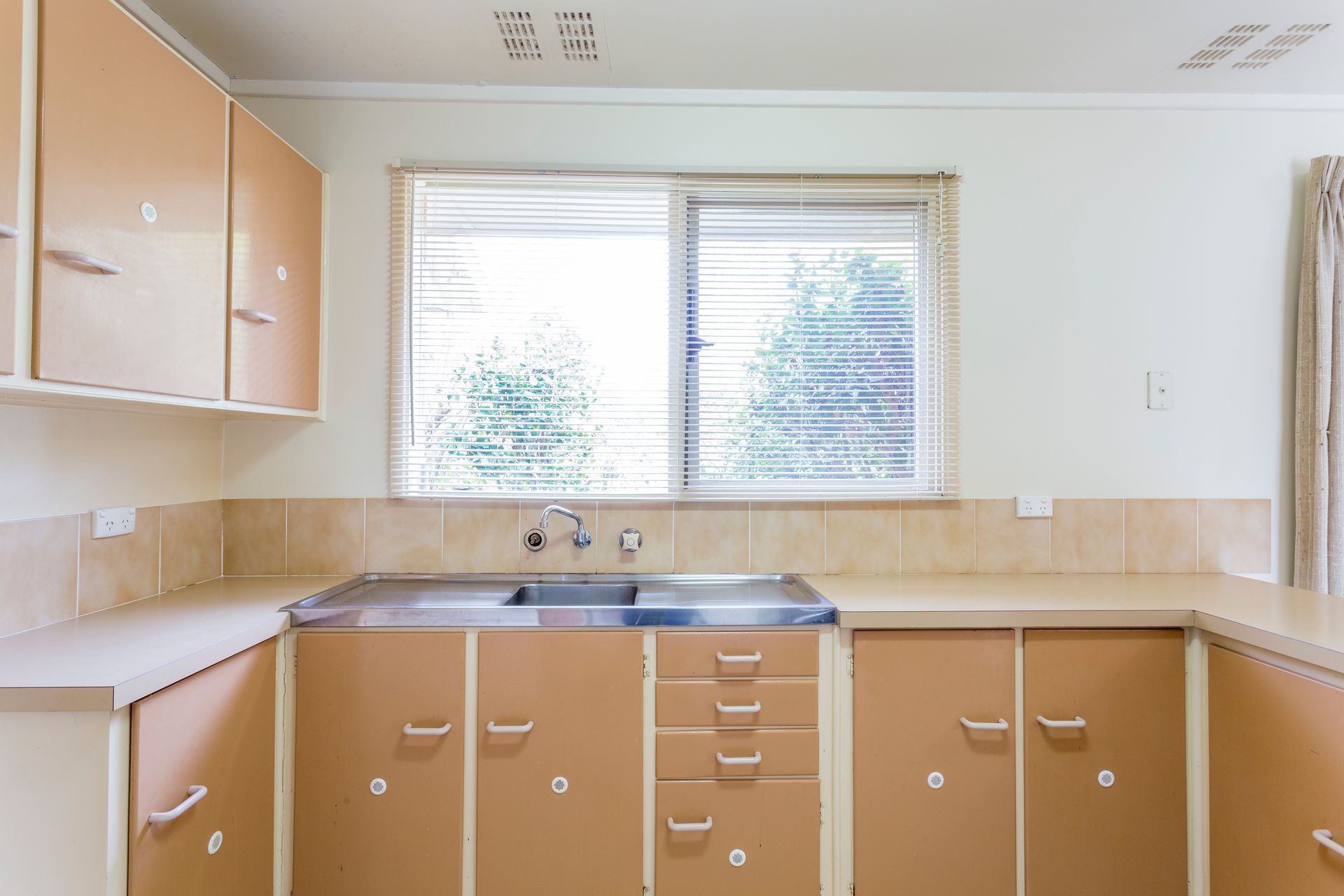 Kitchen with tan cabinets, light countertops, and a window with blinds.