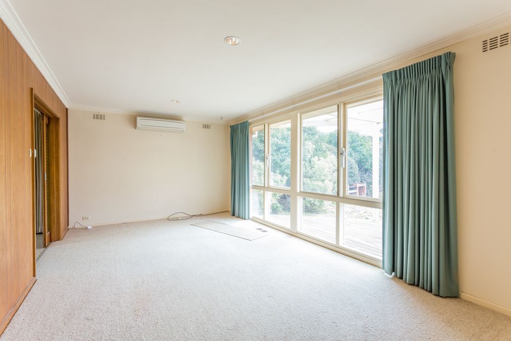 Empty living room with large windows, light carpet, and blue curtains.