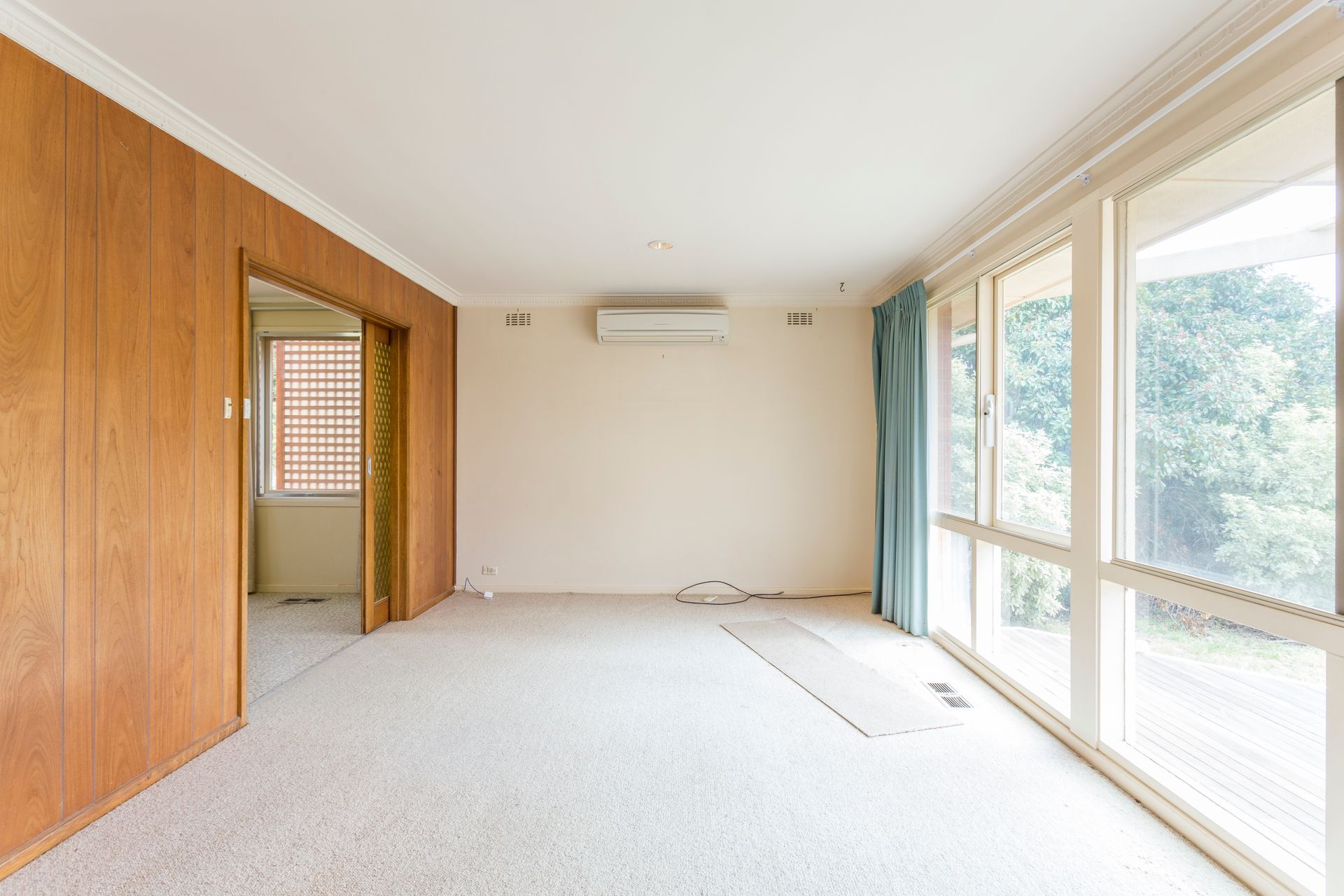 Empty room with light carpet, wood paneling, and large windows.