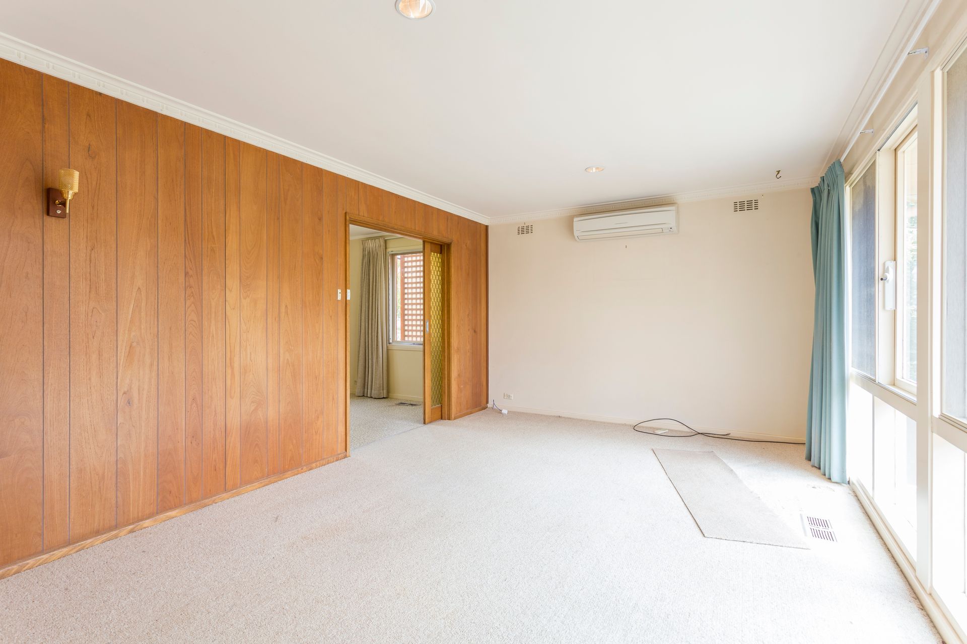 Empty room with wood paneling, white walls, carpet, and large window with curtains.