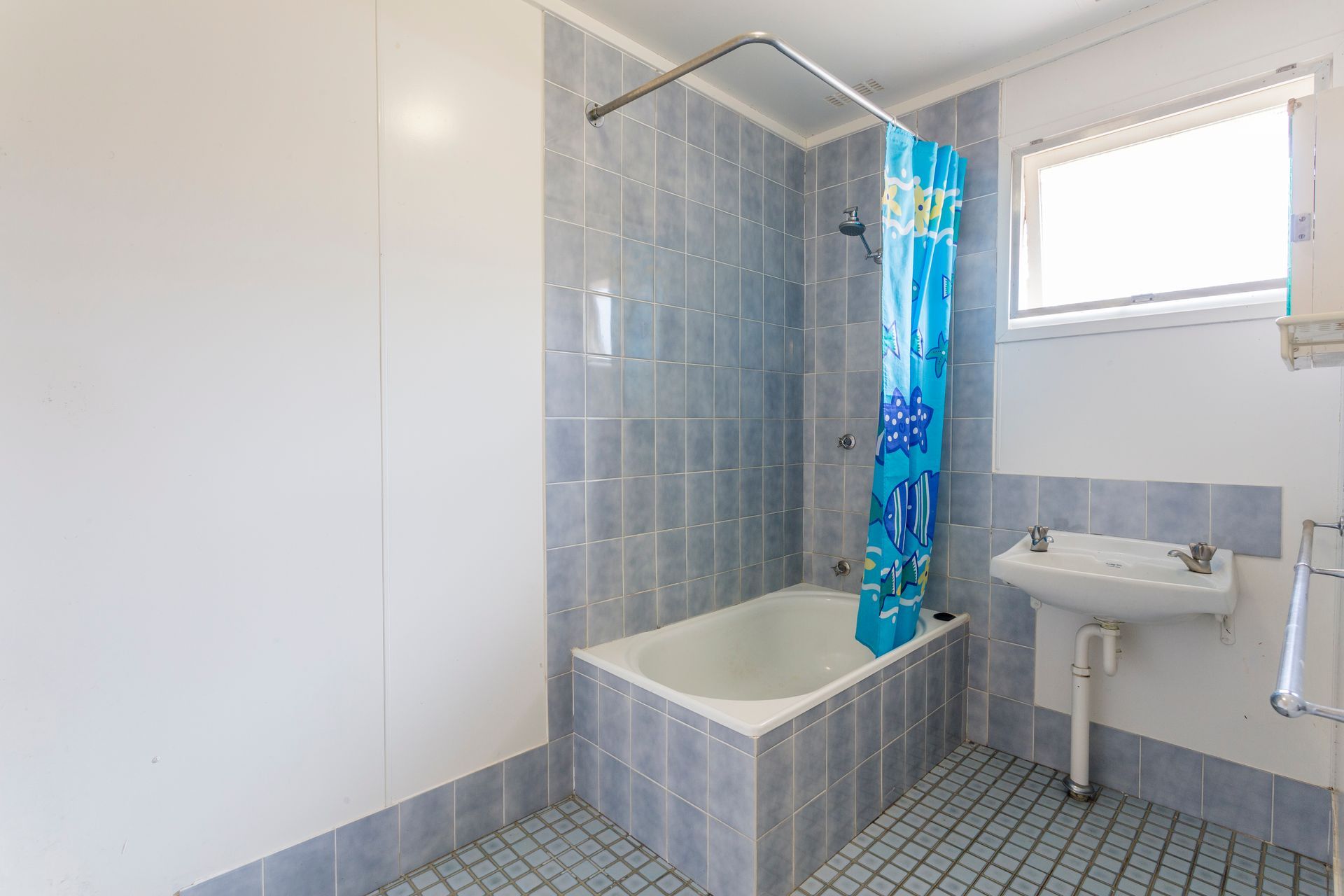 Small bathroom with blue tiled walls, a bathtub, and a window.