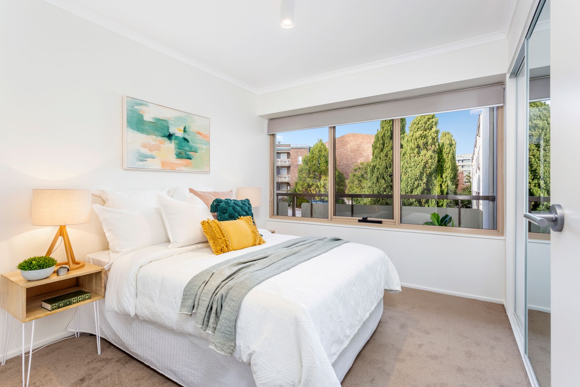 Living room with a beige sofa, two white armchairs, and a glass coffee table in front of a balcony.
