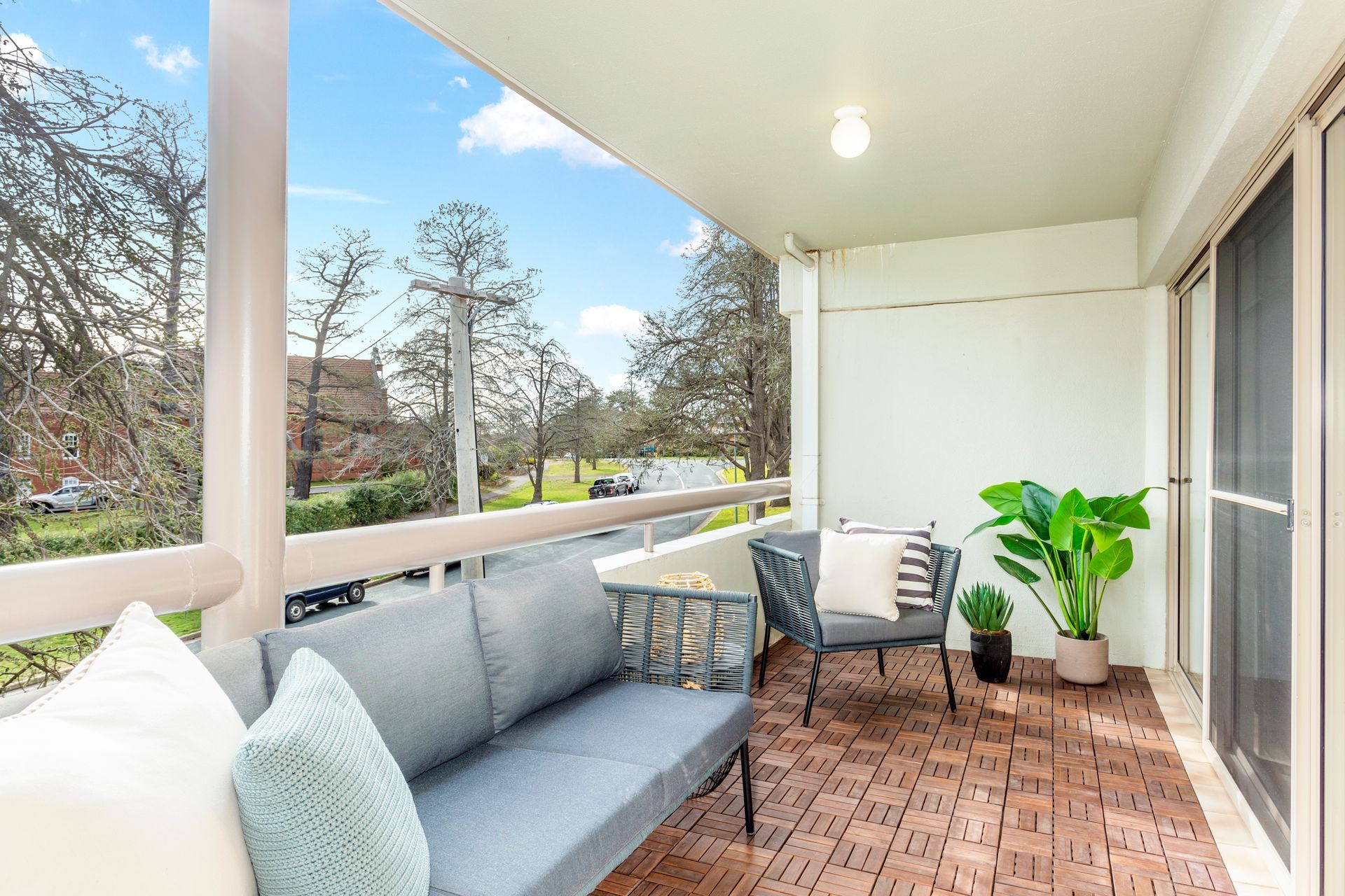 Balcony with grey furniture, plants, and a view of trees and road.