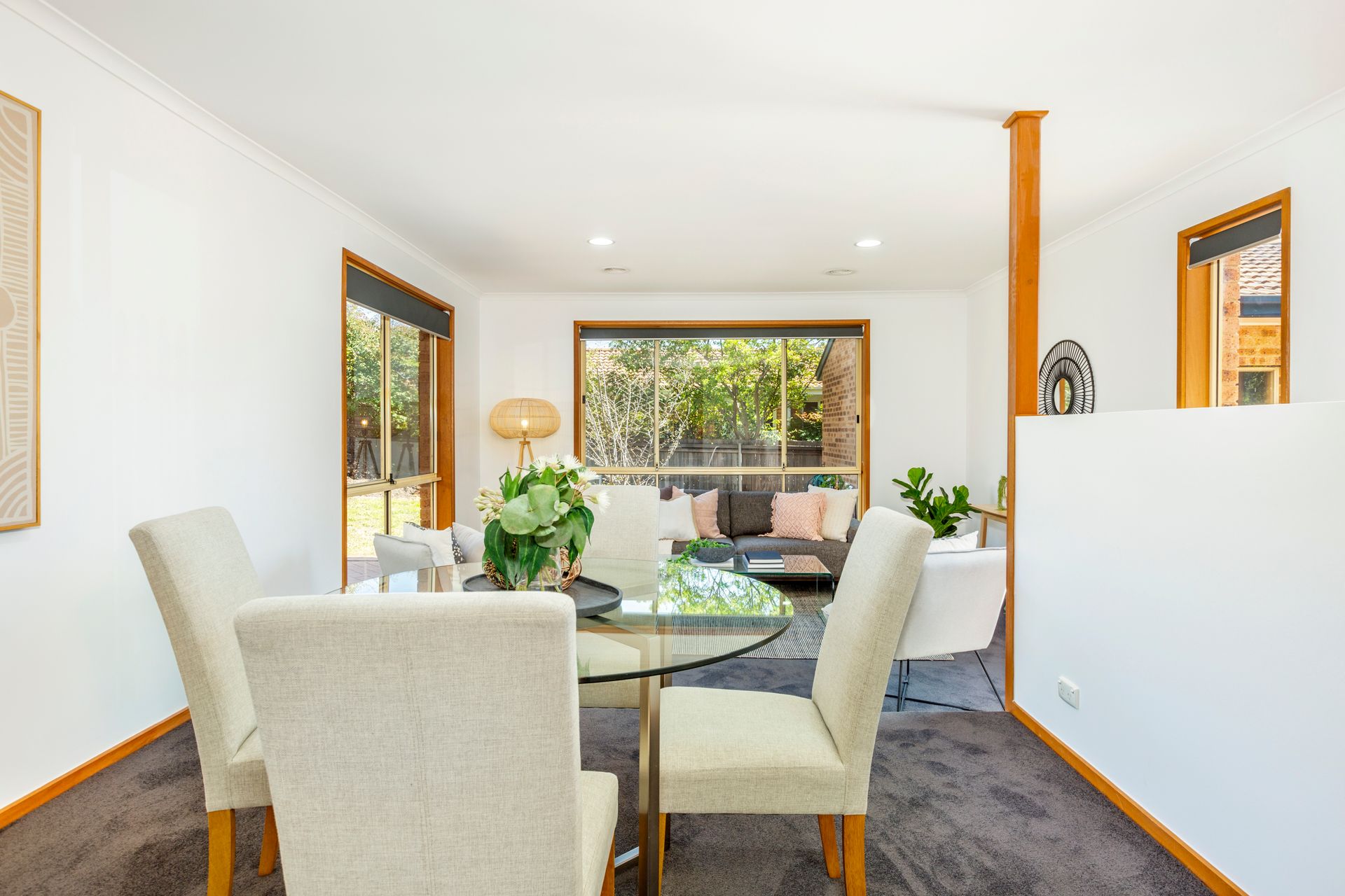Dining room with glass table, four chairs, and a window overlooking greenery.