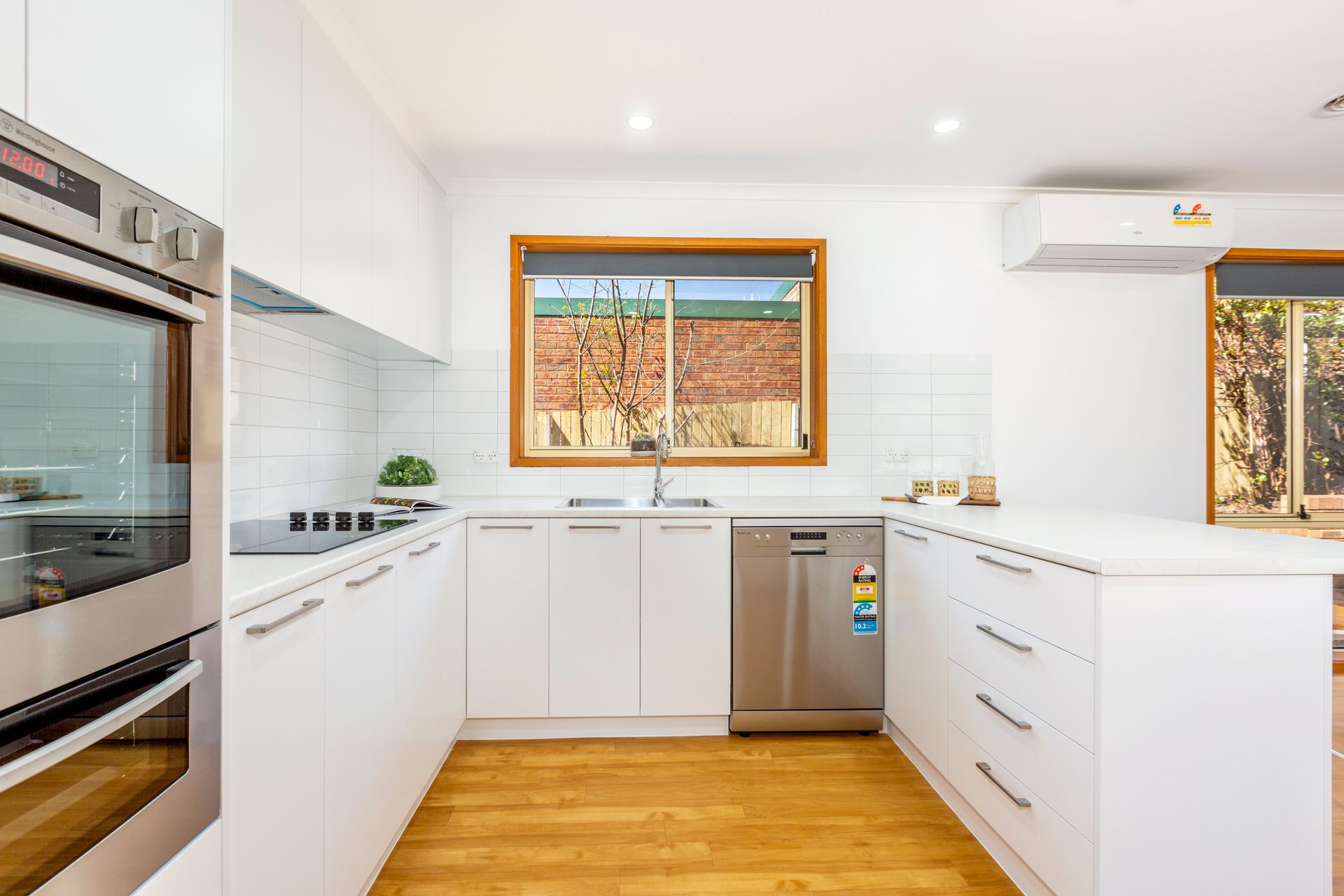 White kitchen with wooden floor, cabinetry, stainless steel appliances, window, and countertop island.