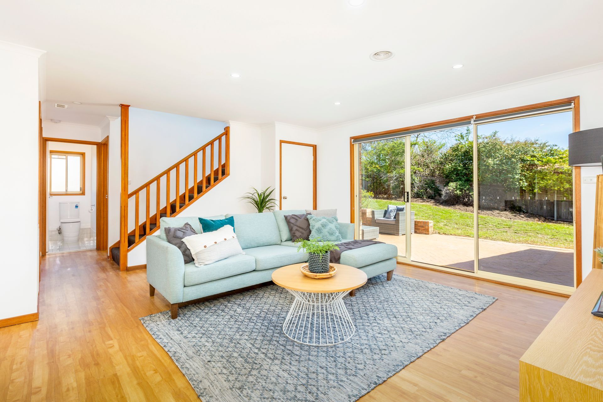 Living room with blue sofa, wooden floors, stairs, and sliding glass doors to a backyard.