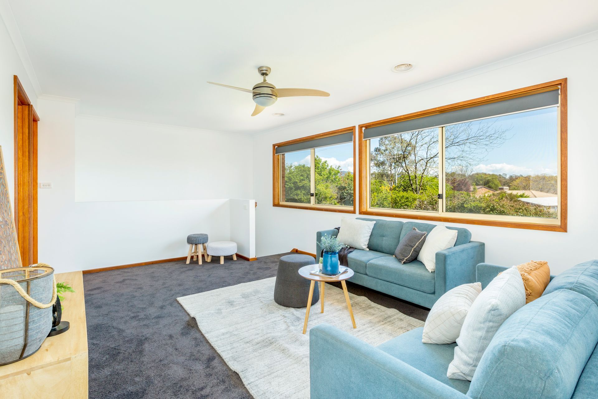 Bedroom with large windows, neutral walls, gray carpet, bed with decorative pillows and a colorful abstract art piece.