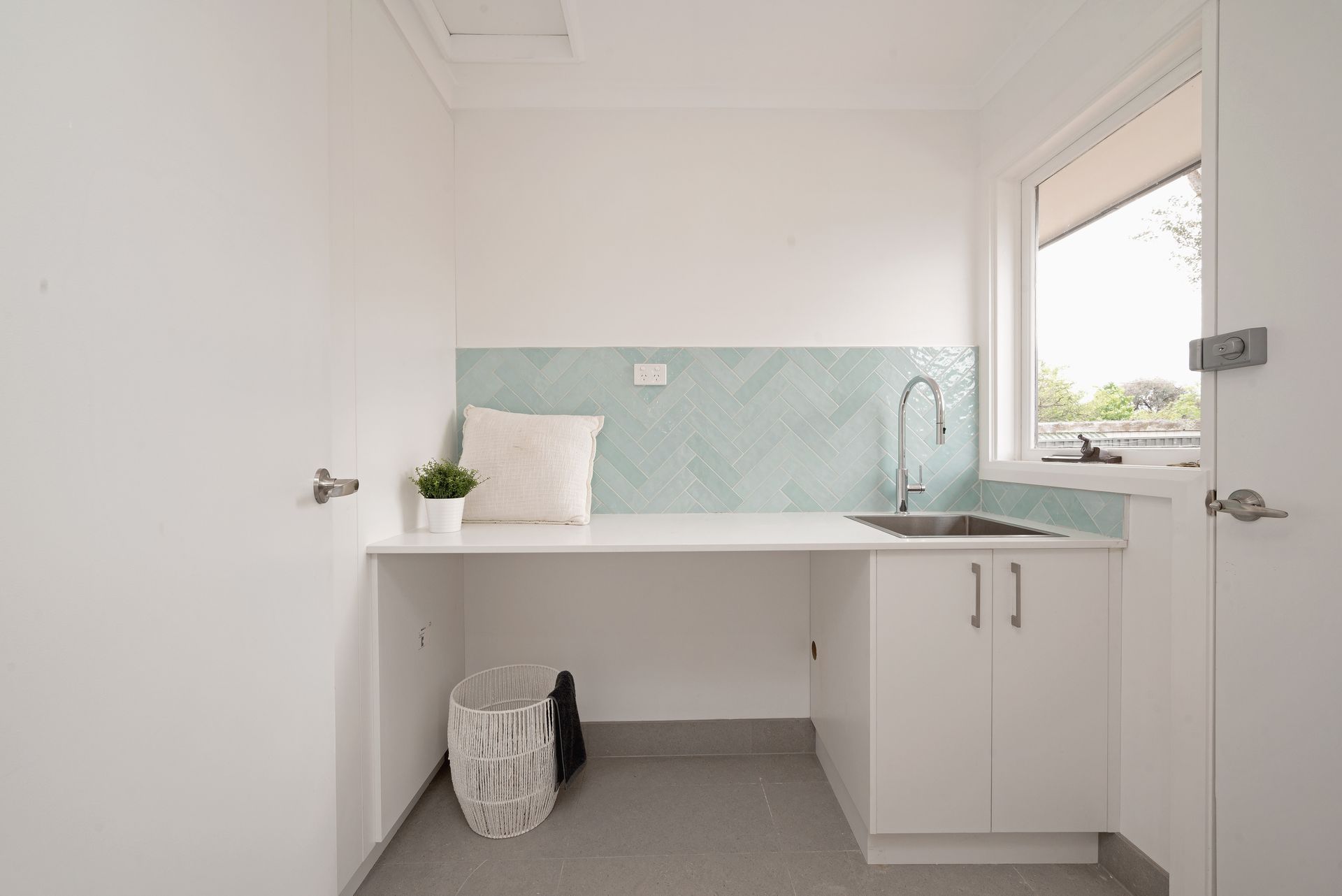 White laundry room with overhead cabinets, black countertop, sink, and shelving.