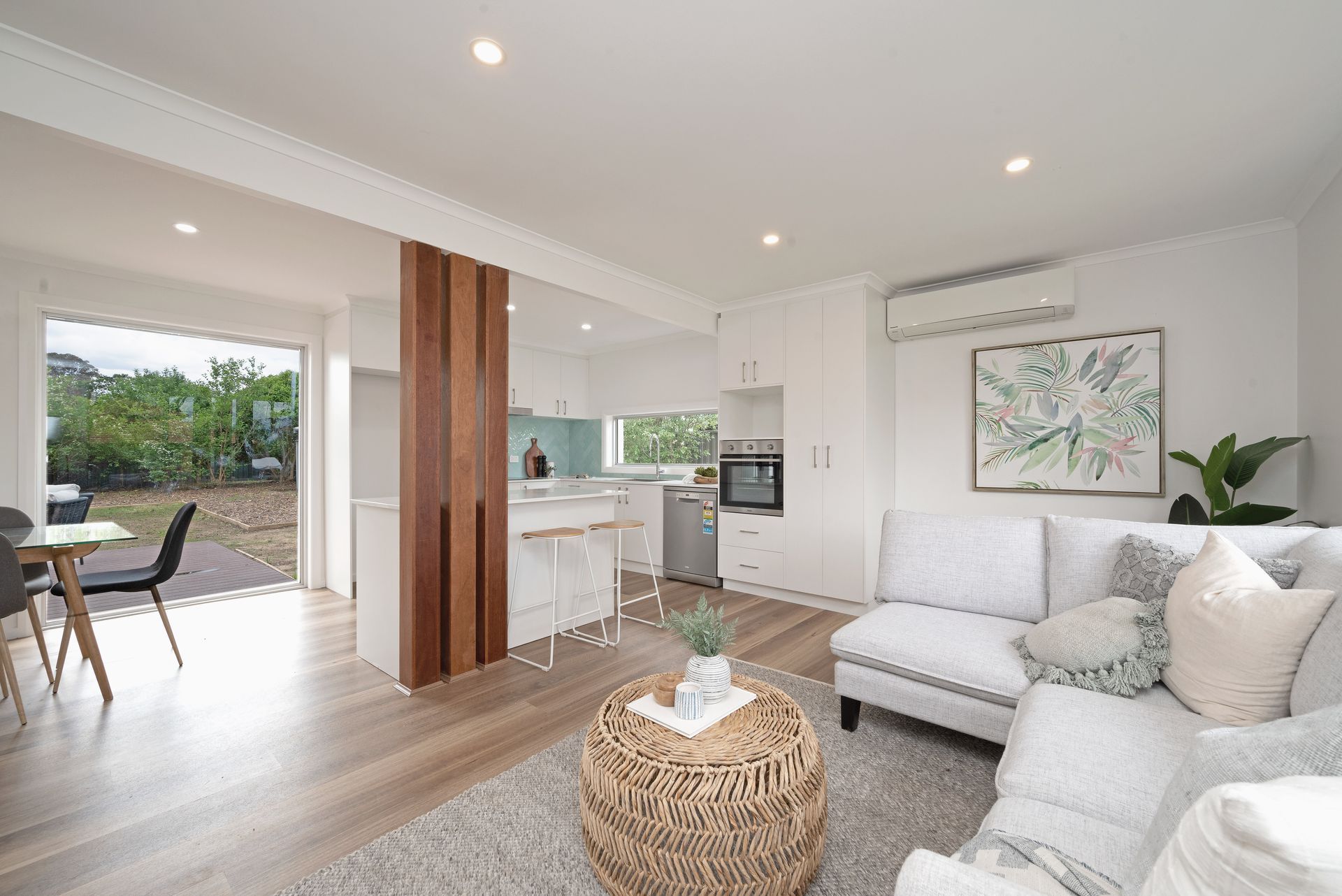 Bedroom with white walls, window, bed with orange and pink accents, two bedside tables, and a potted plant.