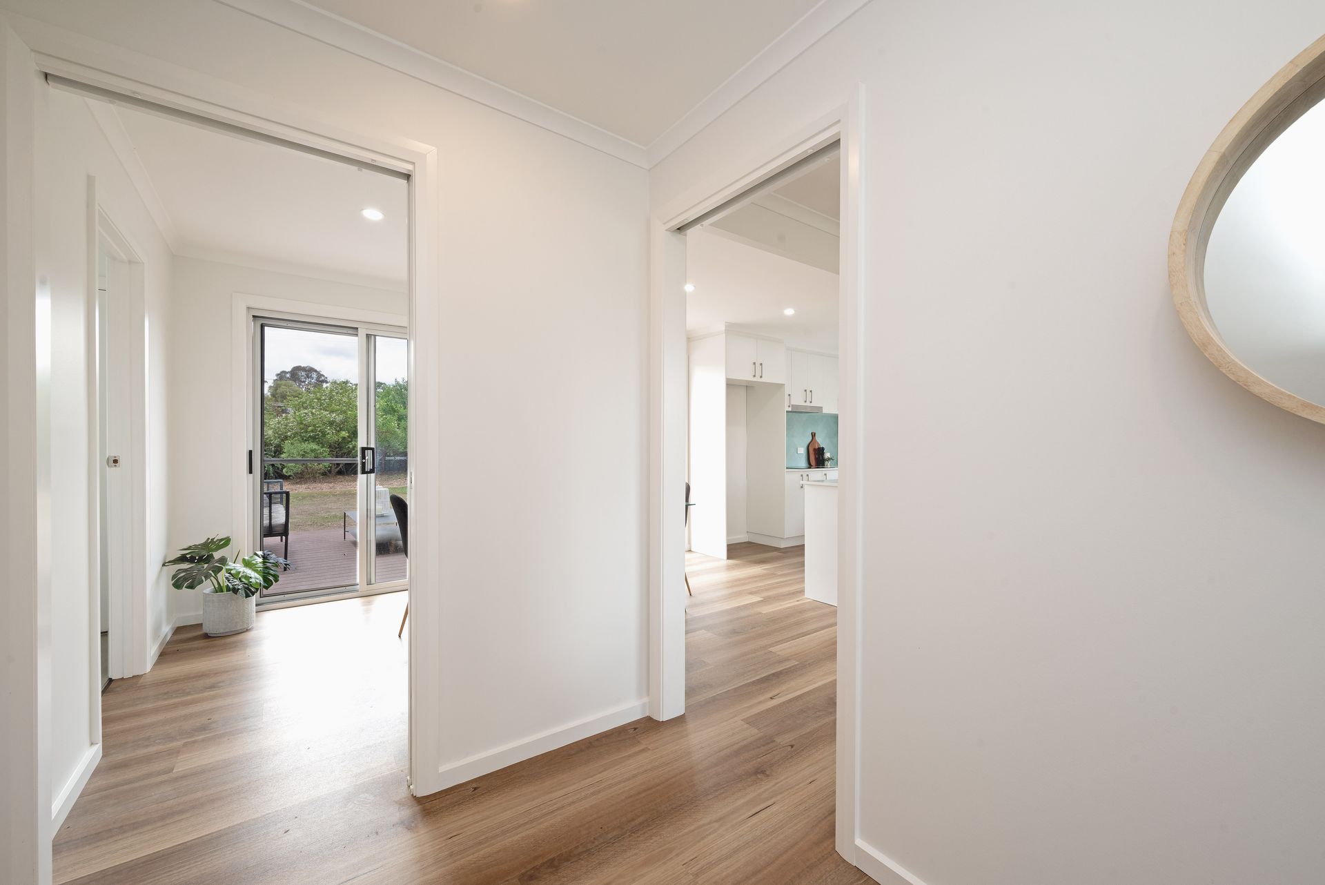 Bedroom with white walls, window, bed with orange and pink accents, two bedside tables, and a potted plant.