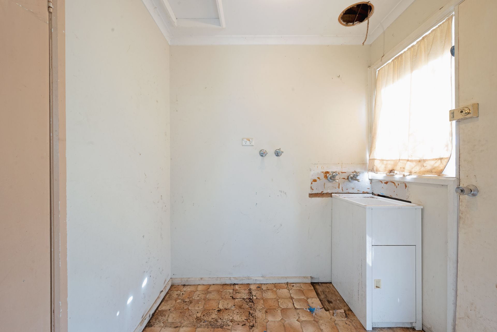 Dilapidated utility room with a sink, counter, and peeling wall tiles.