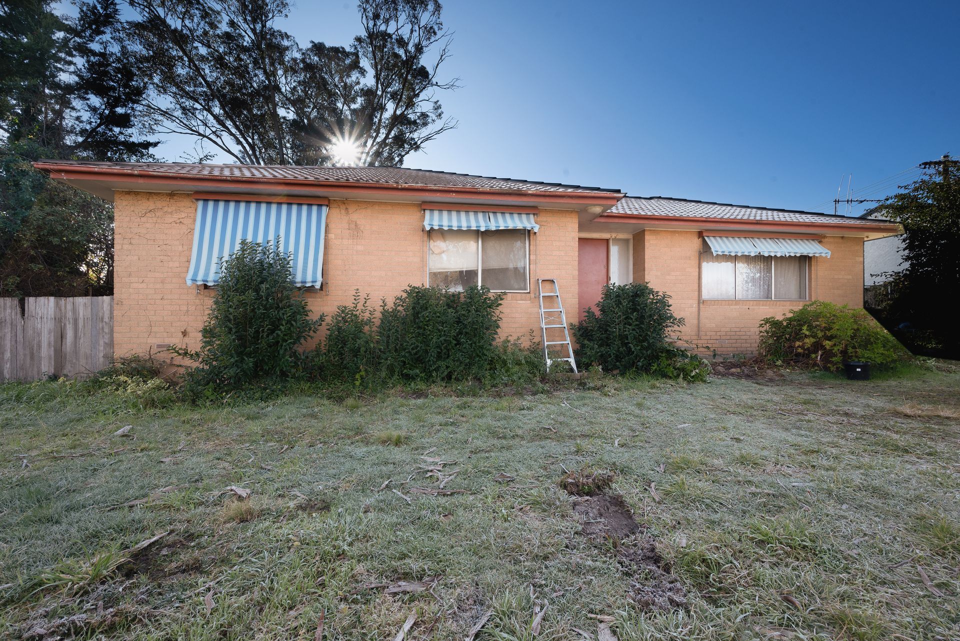 Brick house with overgrown front yard; gray car parked to the side.