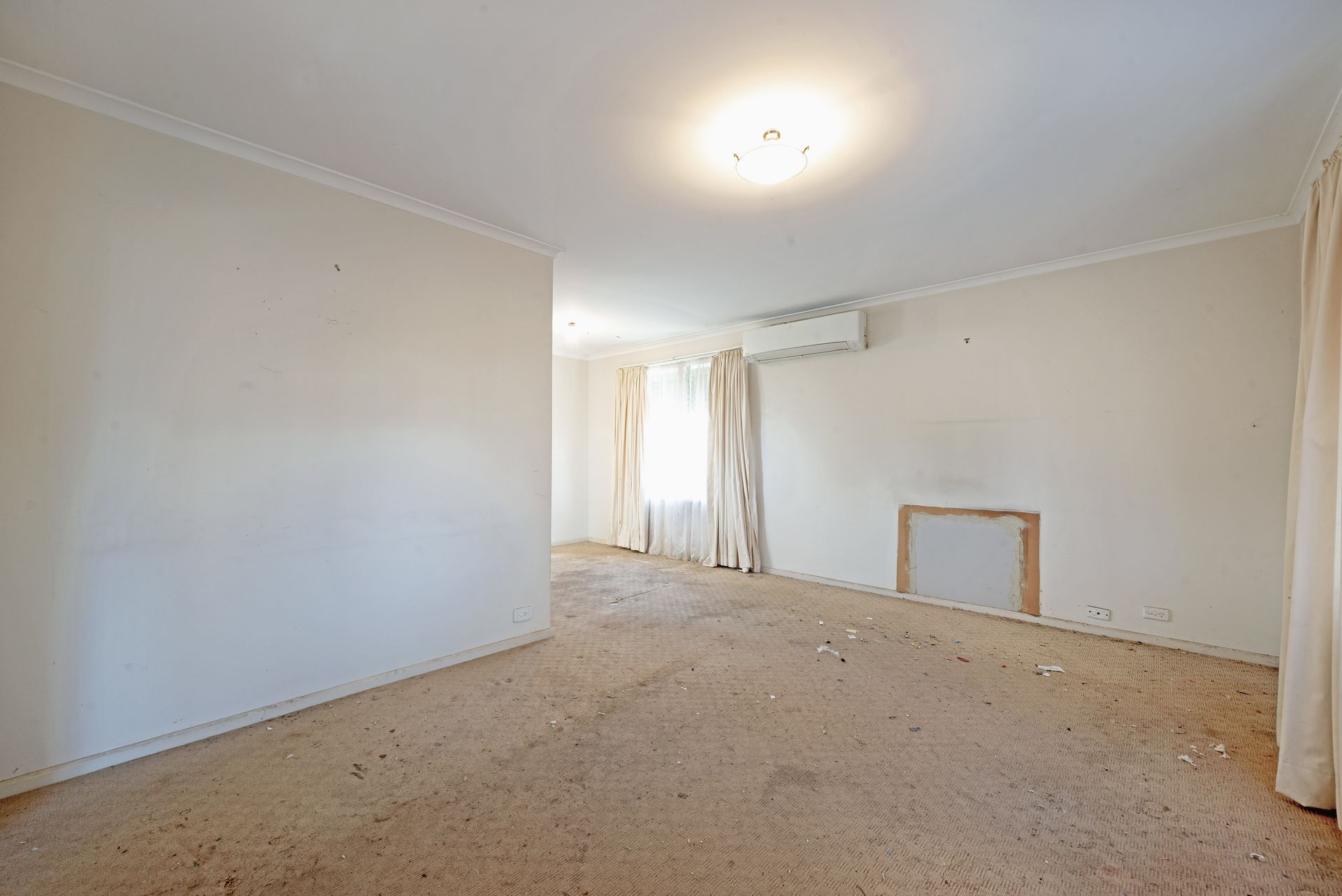 Empty bedroom with a bed, boxes, and a window. Beige walls and carpet.