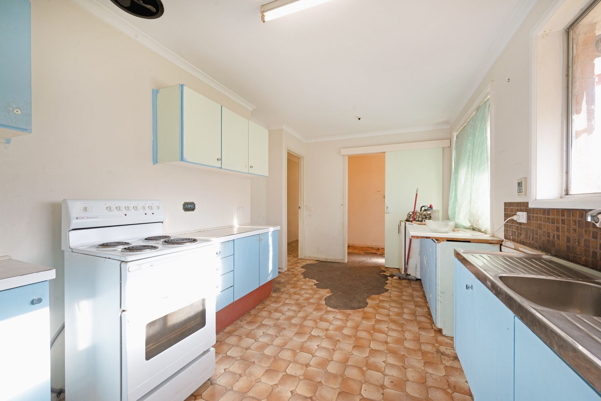 Dilapidated utility room with a sink, counter, and peeling wallpaper.