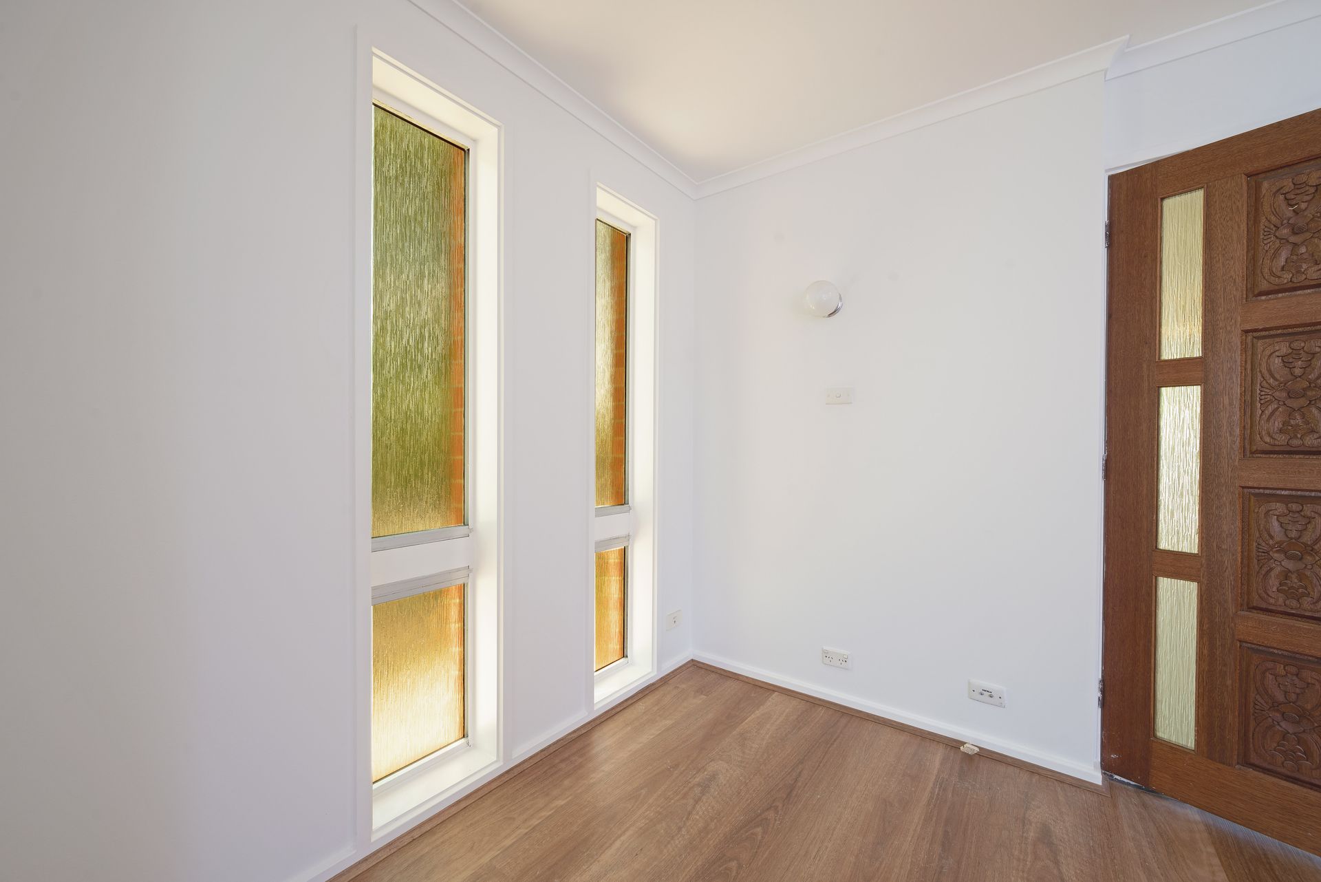 Empty room with two tall windows, a decorative wooden door, and wood-look flooring.