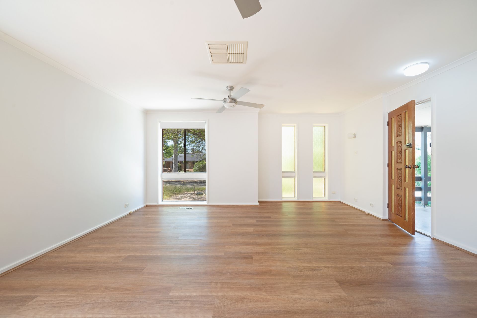 Empty room with wood floors, white walls, two windows, ceiling fan, and wooden door.