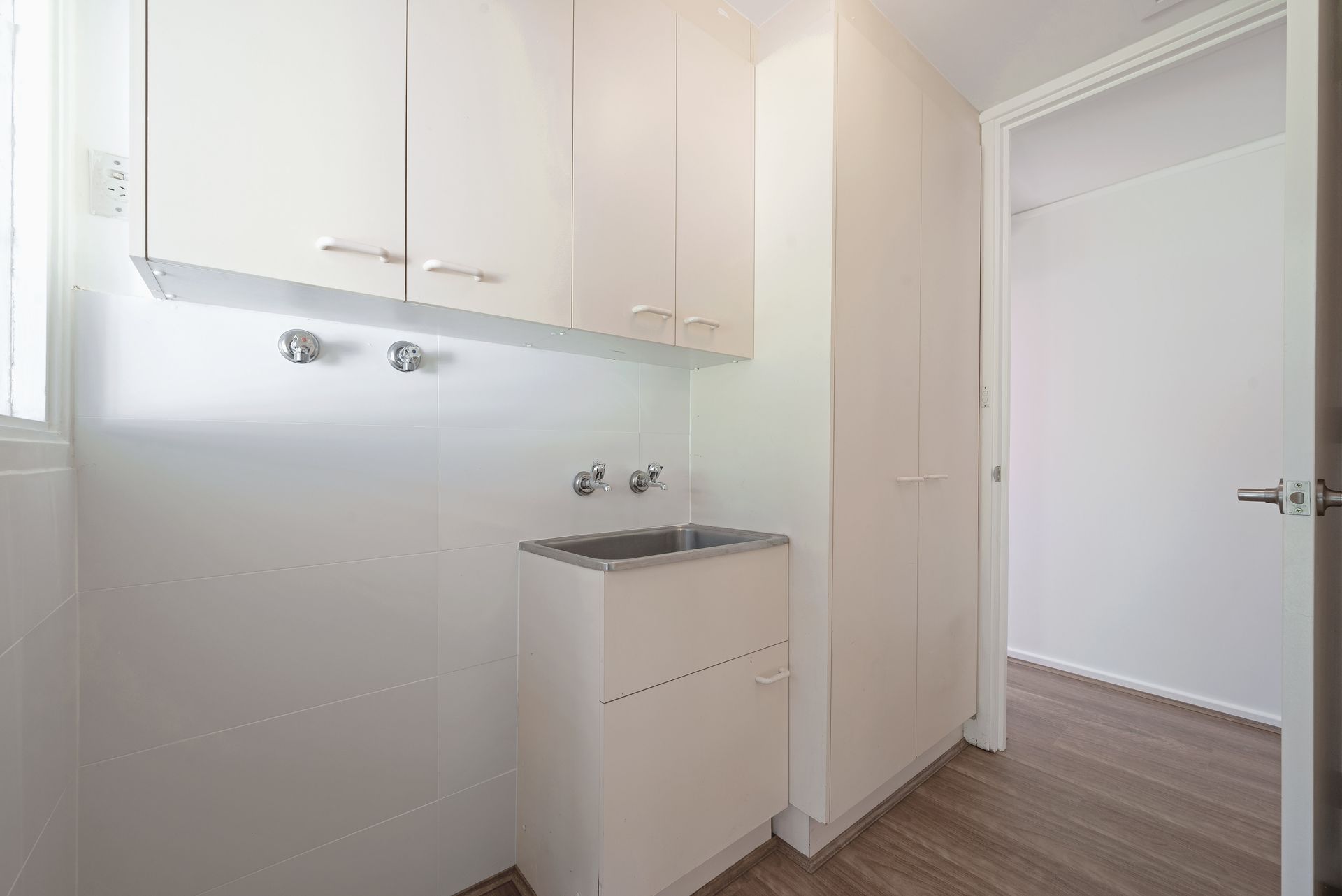 White laundry room with overhead cabinets, sink, and tall storage cabinet.