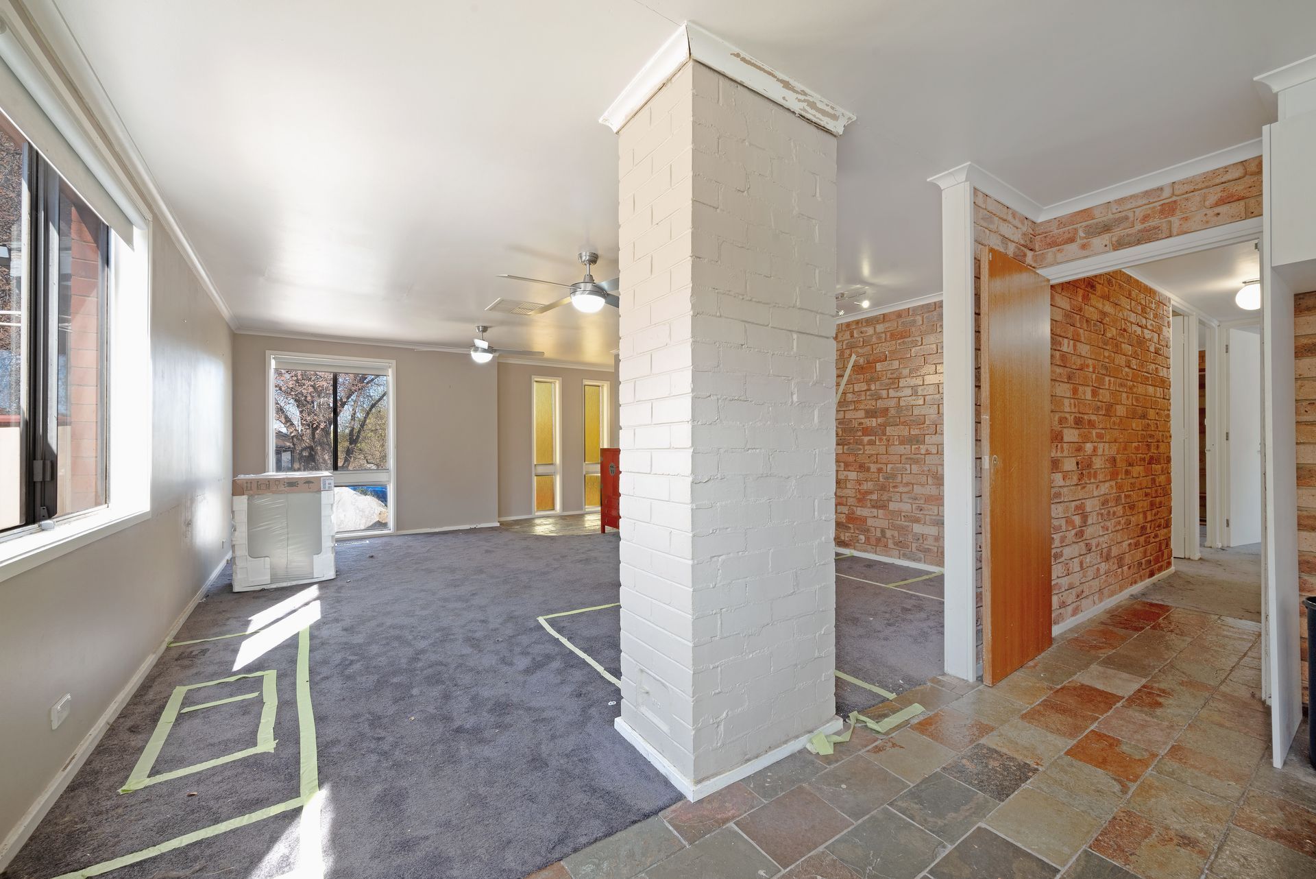 Open-concept living space with gray carpet, a brick pillar, and a doorway with brick accent walls.