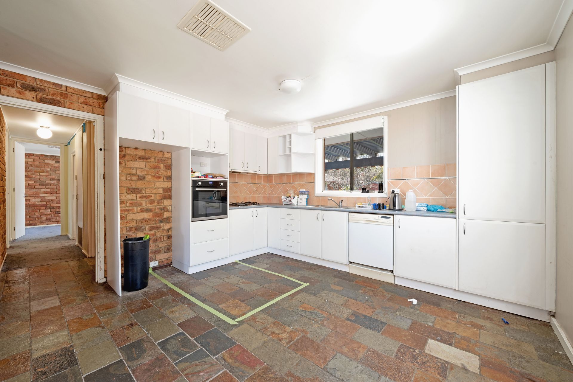 Kitchen with white cabinets, appliances, and brick wall. Slate tile floor.