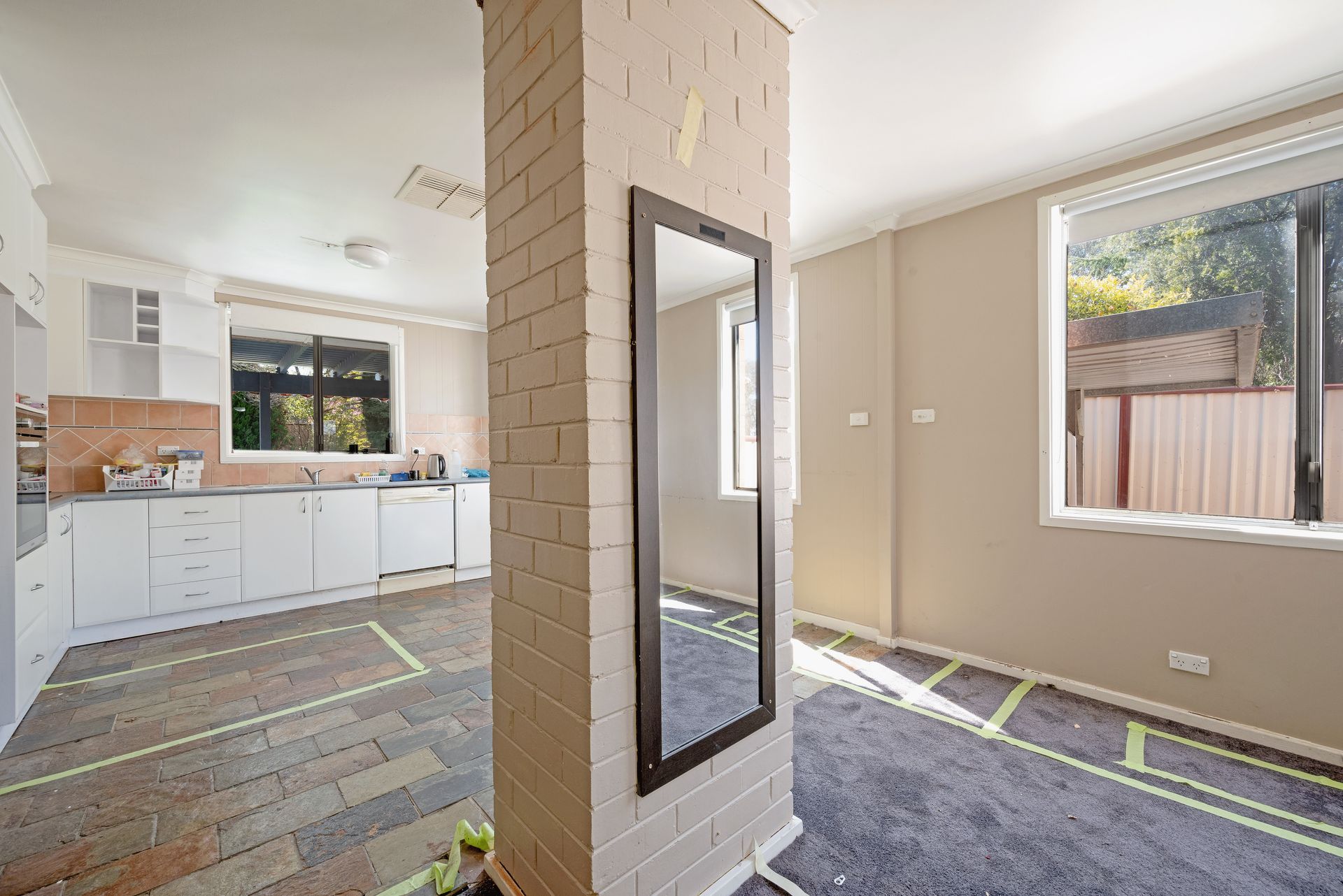 Open-plan interior with exposed brick wall, carpeted floor, and kitchen in the background.