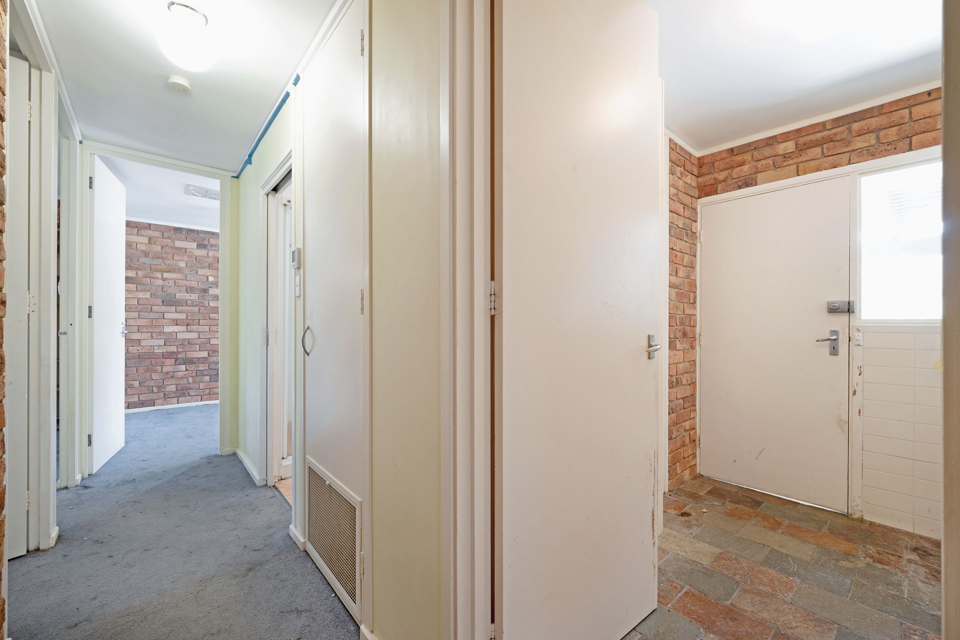 Open-plan interior with exposed brick wall, carpeted floor, and kitchen in the background.