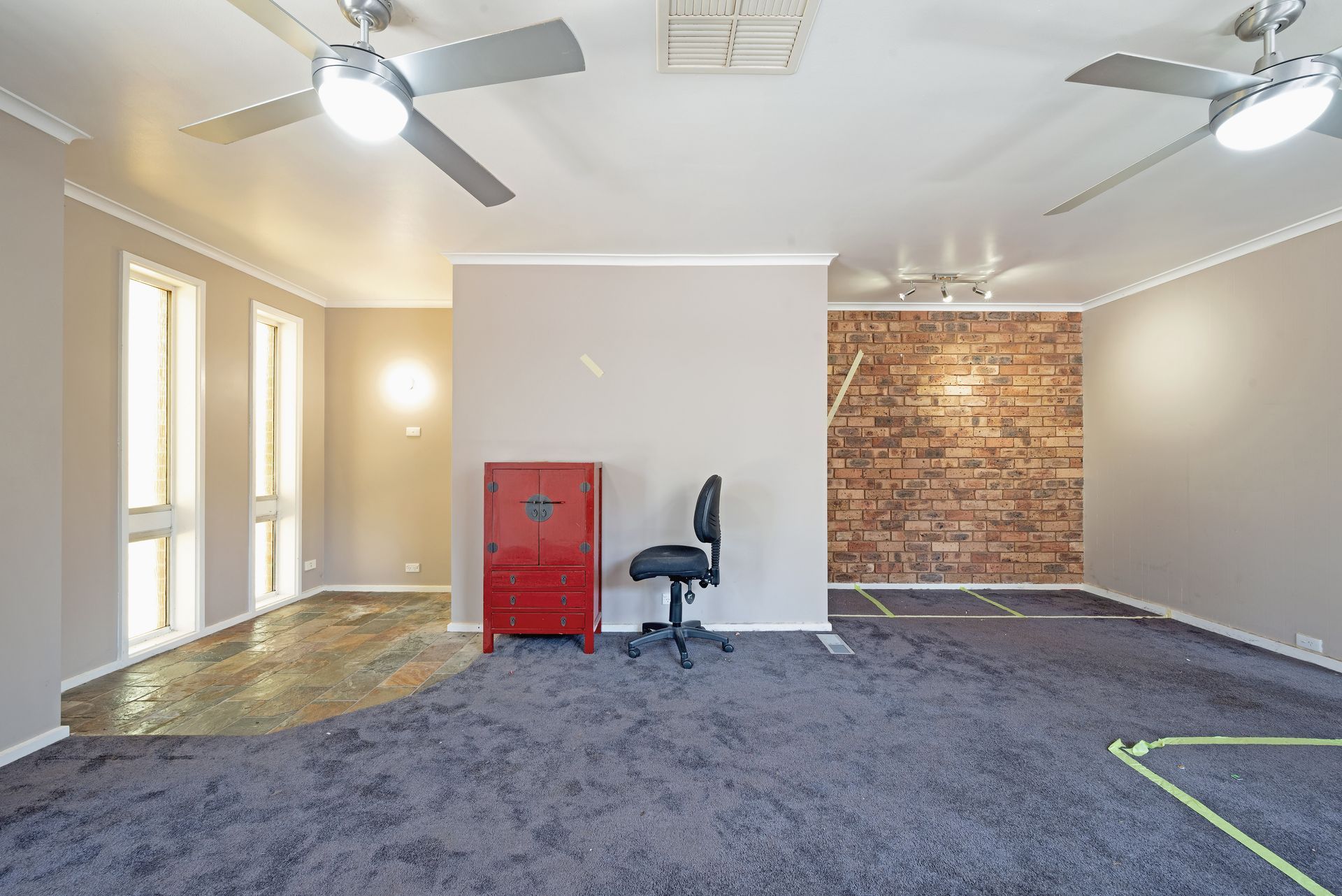 Empty room with dark gray carpet, two ceiling fans, red cabinet, and a black office chair.