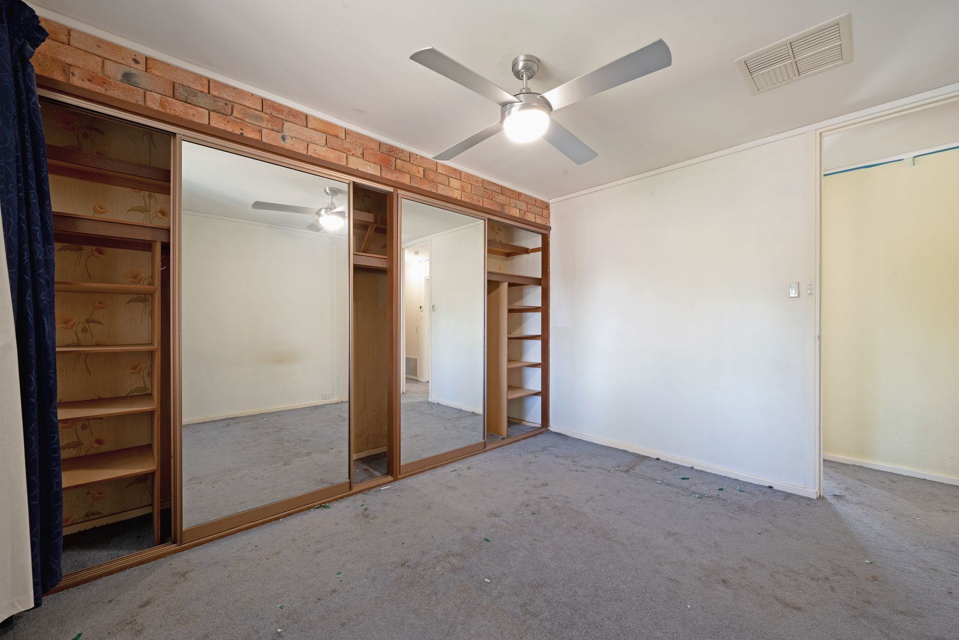 Open-plan interior with exposed brick wall, carpeted floor, and kitchen in the background.