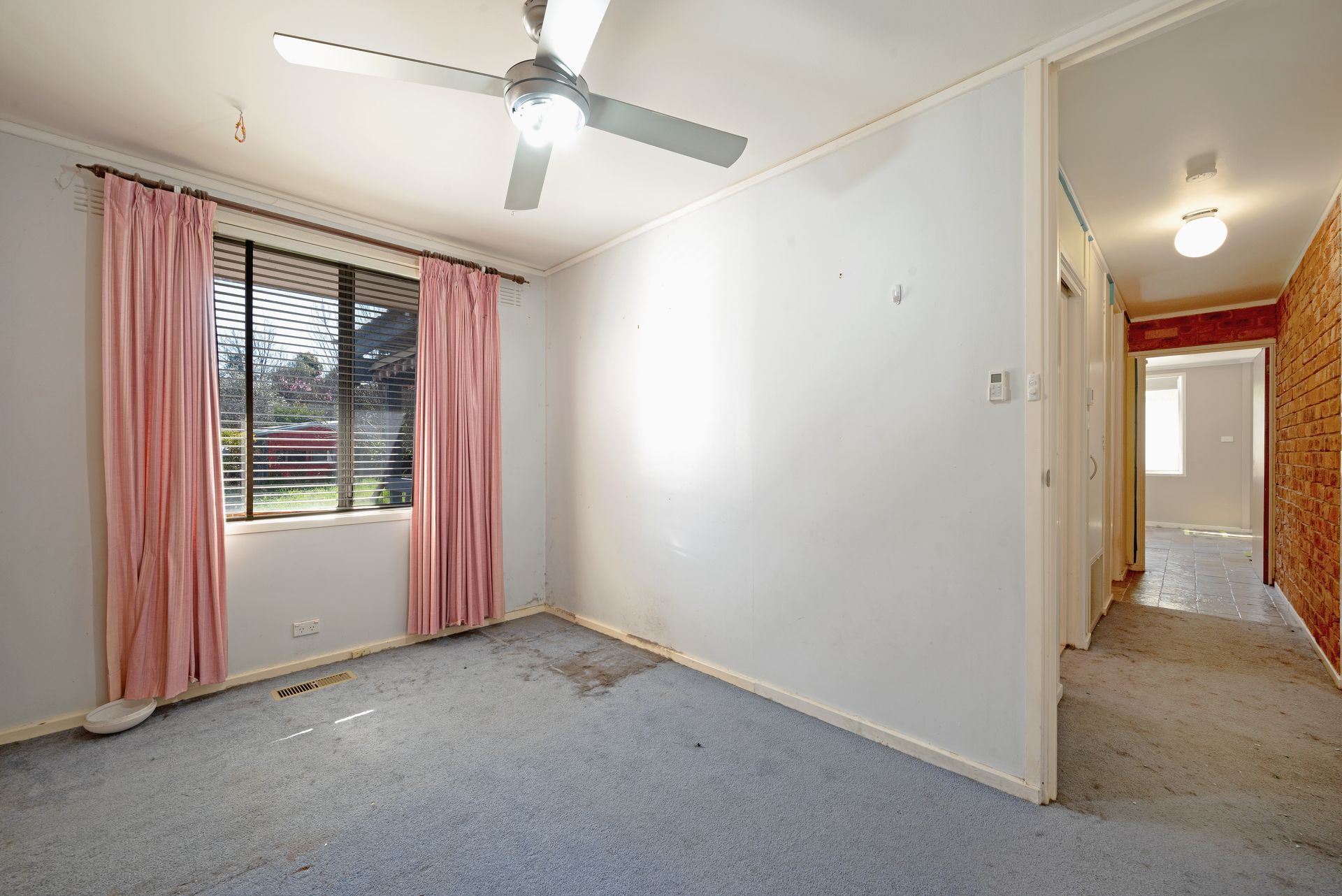 Bedroom with dusty blue carpet, pink curtains, a ceiling fan, and a hallway entrance.