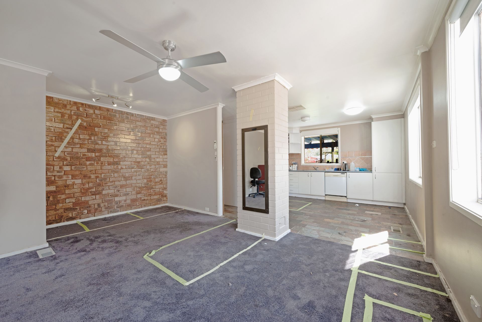Open-plan interior with exposed brick wall, carpeted floor, and kitchen in the background.