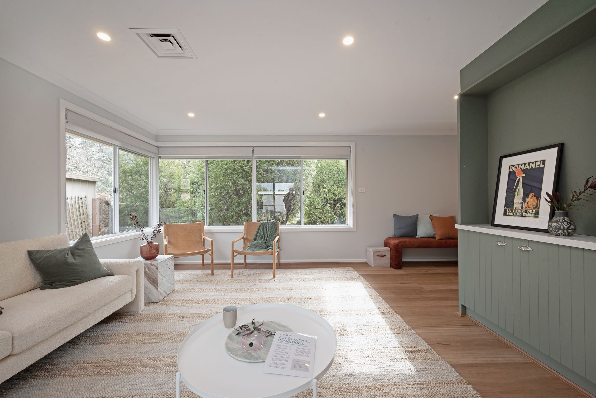 Living room with white sofa, rug, windows, wooden floor, and built-in green cabinetry.