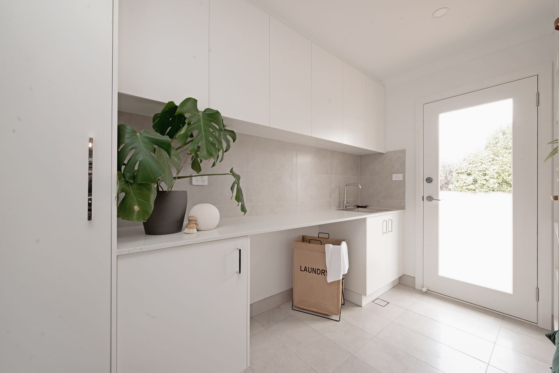 White laundry room with cabinets, counter, window, and shelves.
