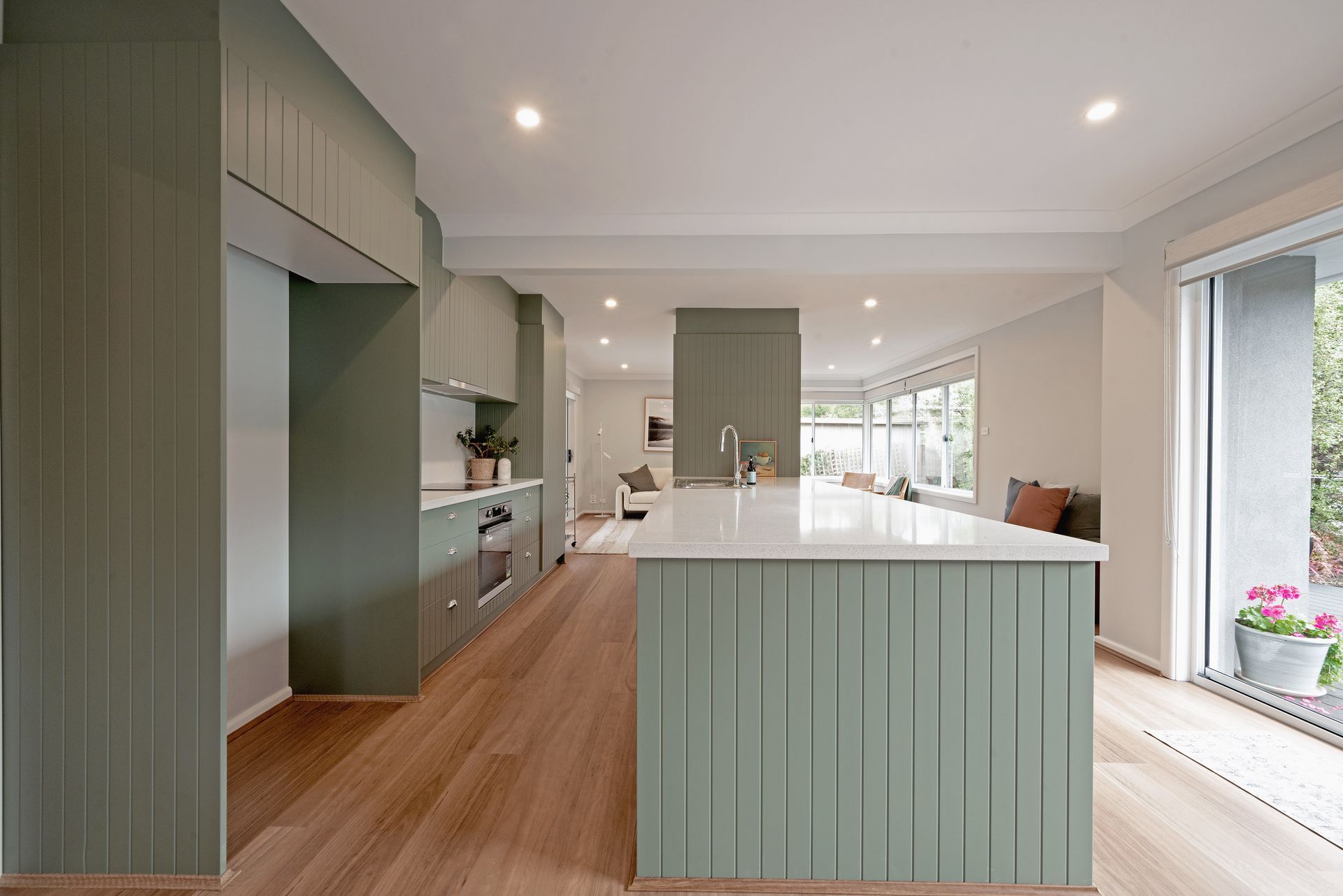 Modern kitchen with green paneling, white countertops, and wooden floors.