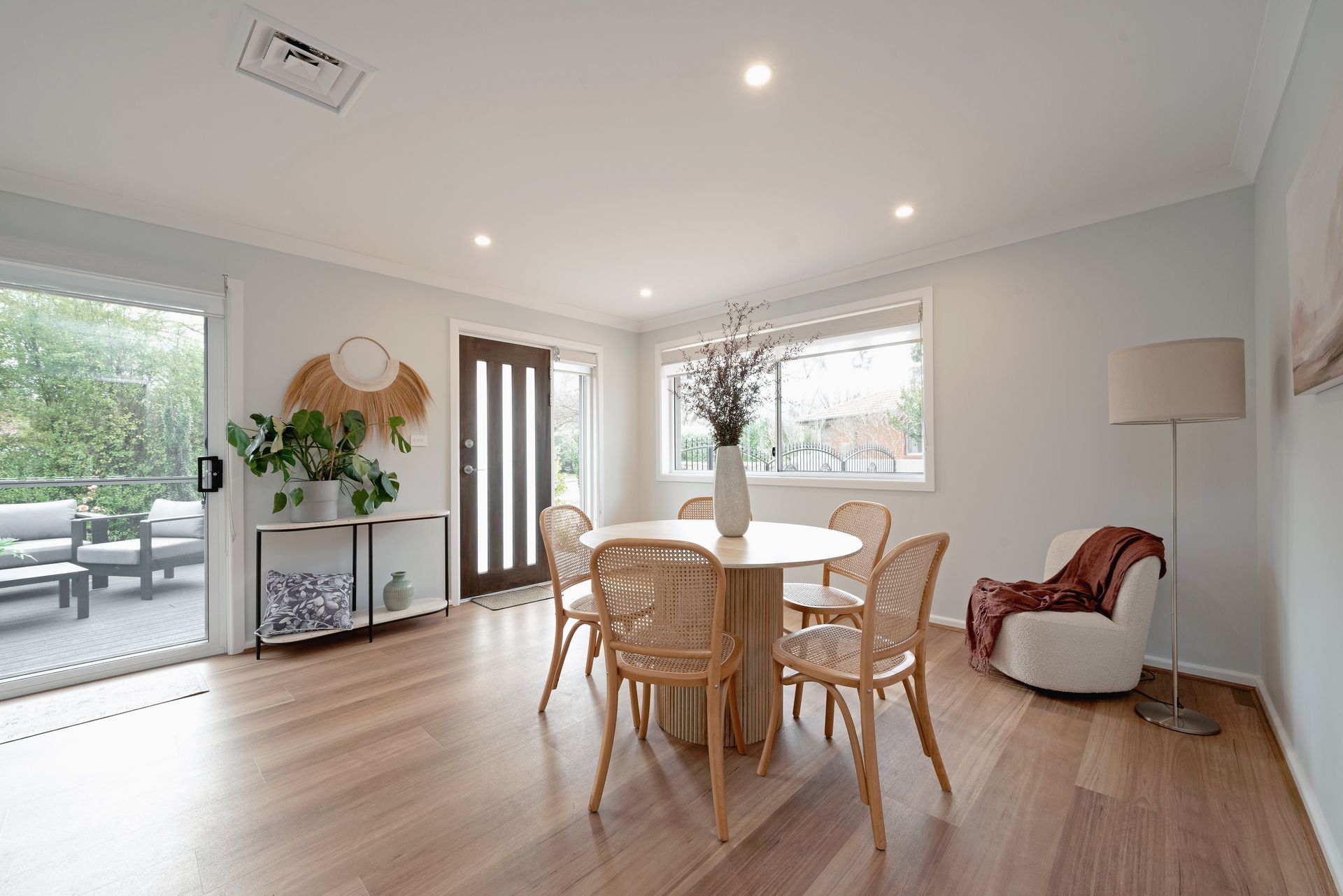 Dining room with round table, rattan chairs, and sliding glass doors to a deck. Light wood floors and neutral walls.