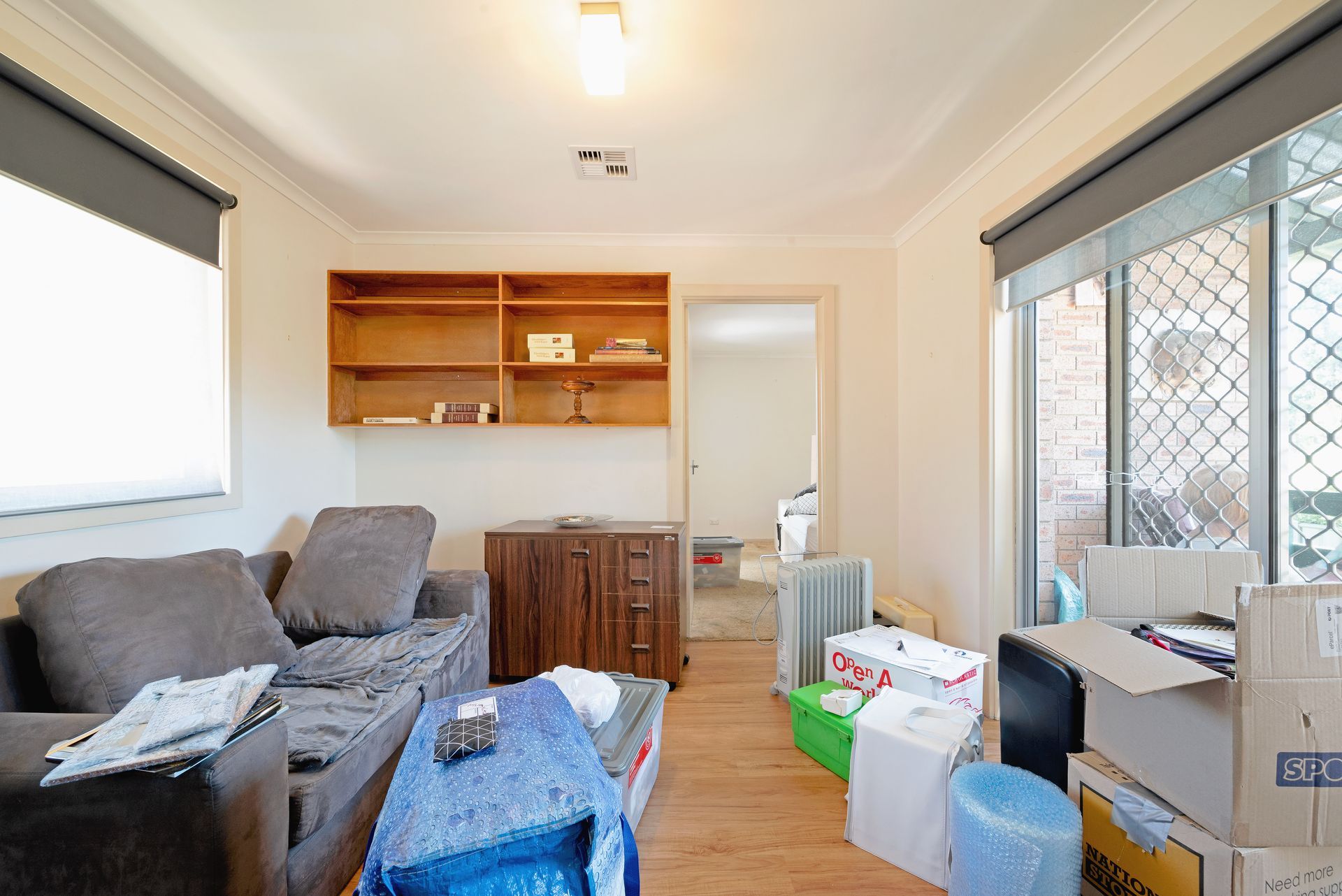 Living room with couch, shelves, boxes; natural light streams in.