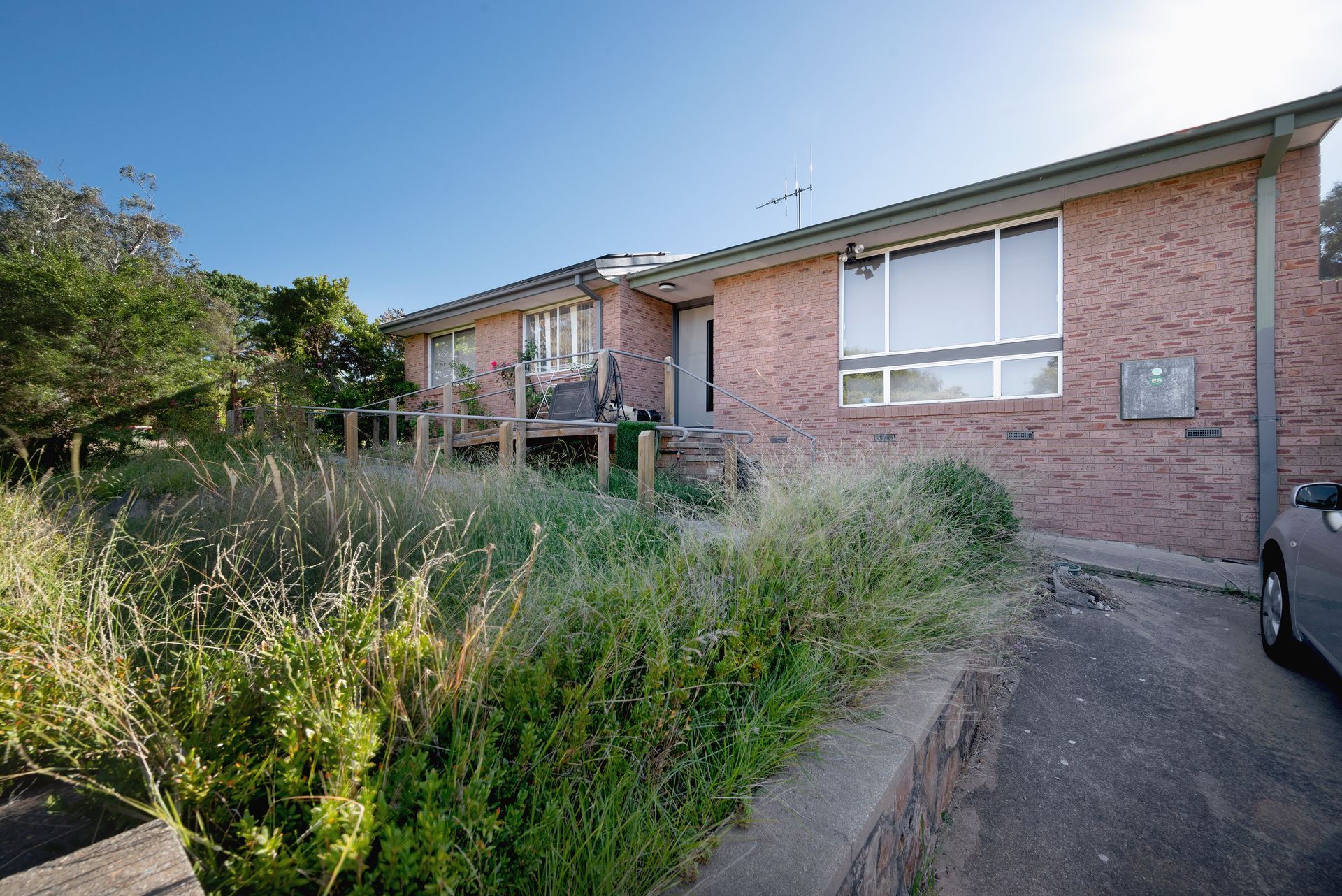 Brick house with overgrown front yard; gray car parked to the side.