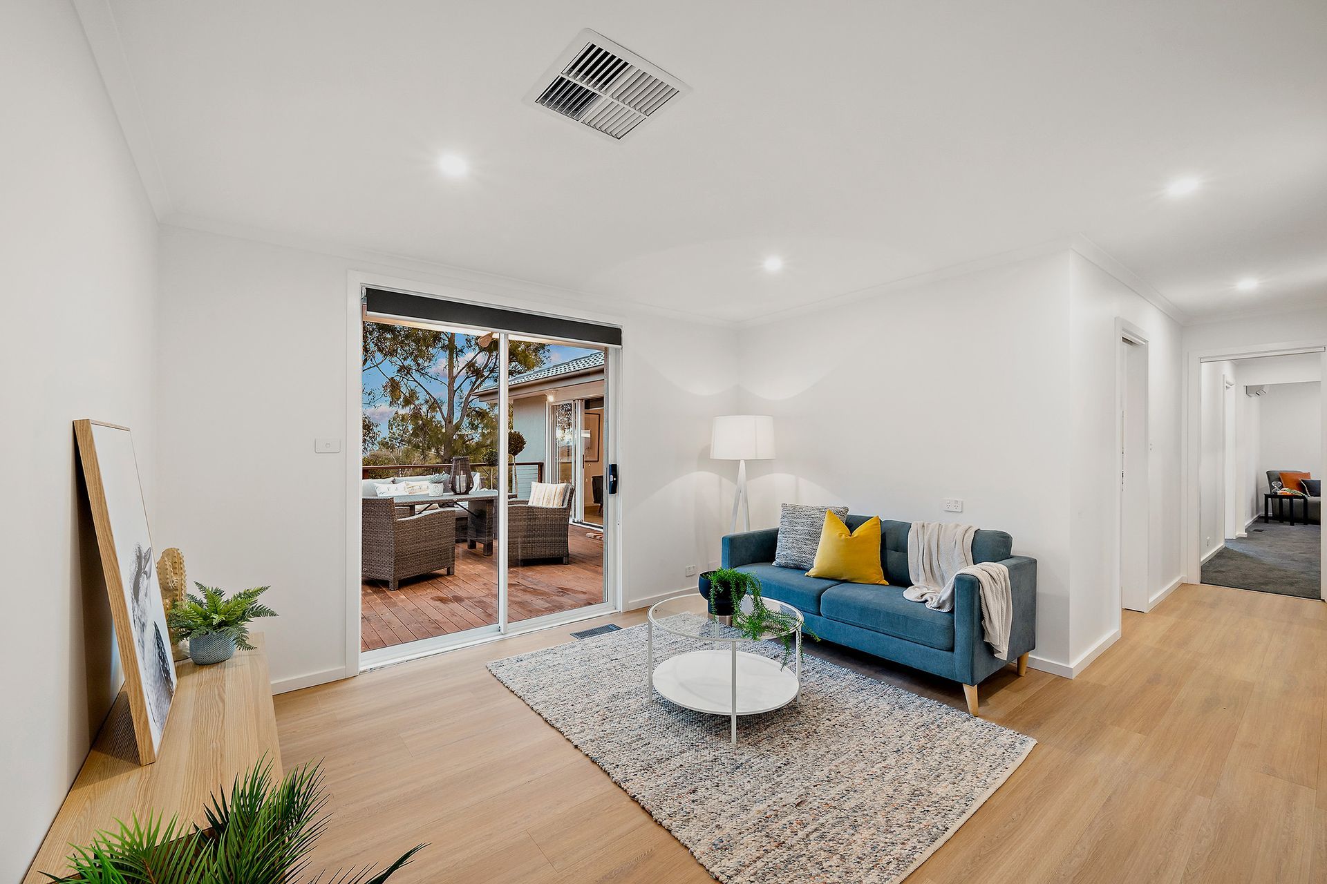 Dining room with wooden table, gray chairs, window, art, and plant. Light wood flooring and white walls.