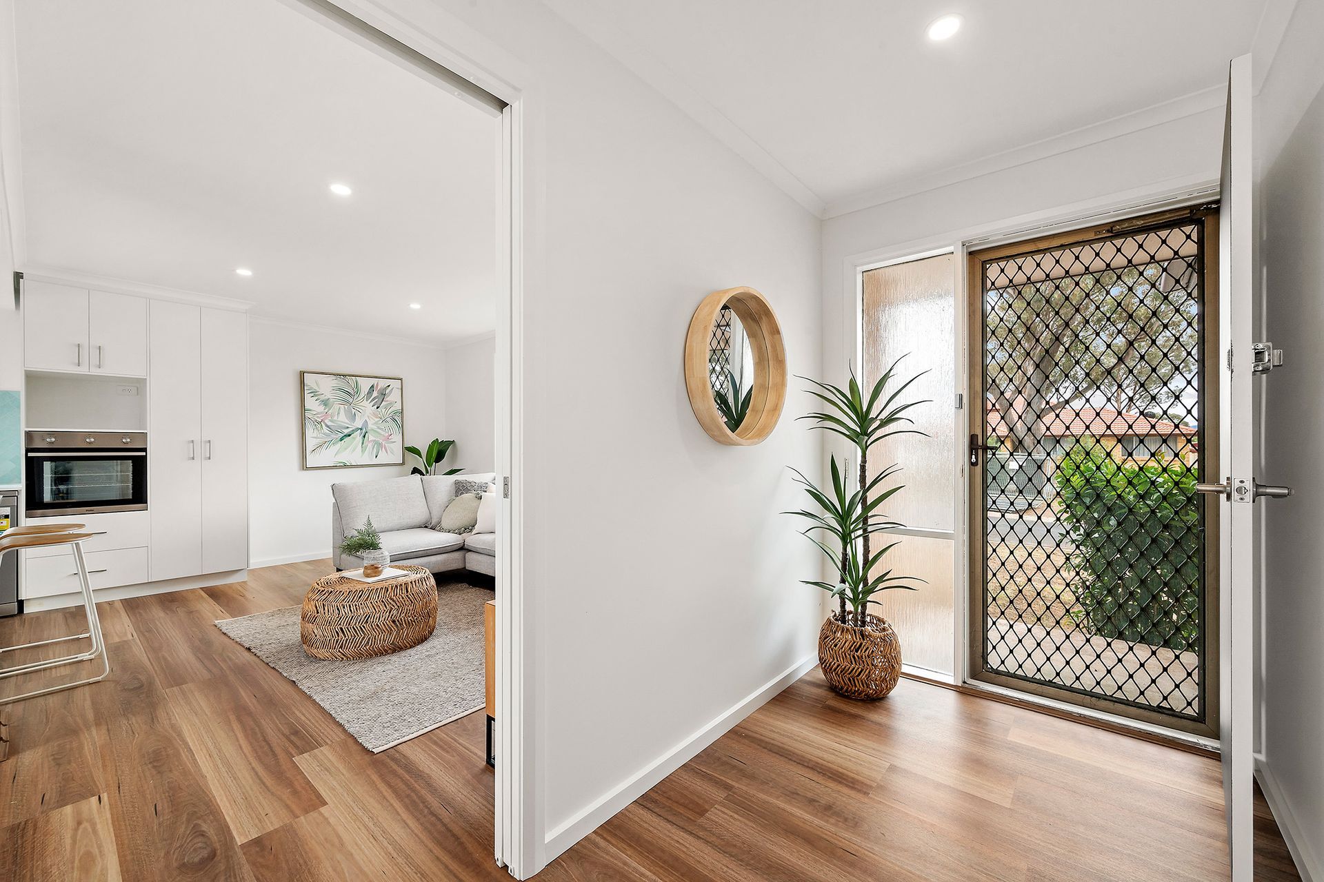 Hallway with hardwood floor, white walls, open to living area, security door, and decorative mirror.